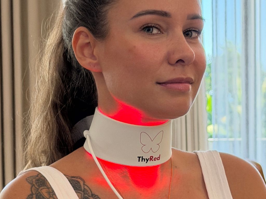 Woman wearing a white "ThyRed" neck collar emitting red light on her throat.