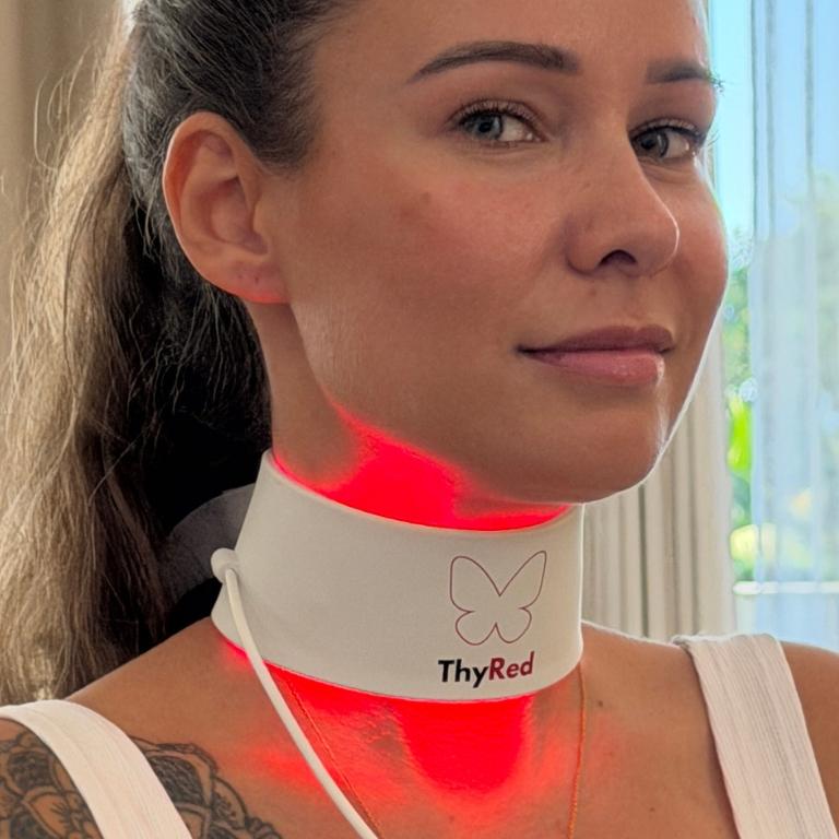 Woman wearing a white "ThyRed" neck collar emitting red light on her throat.