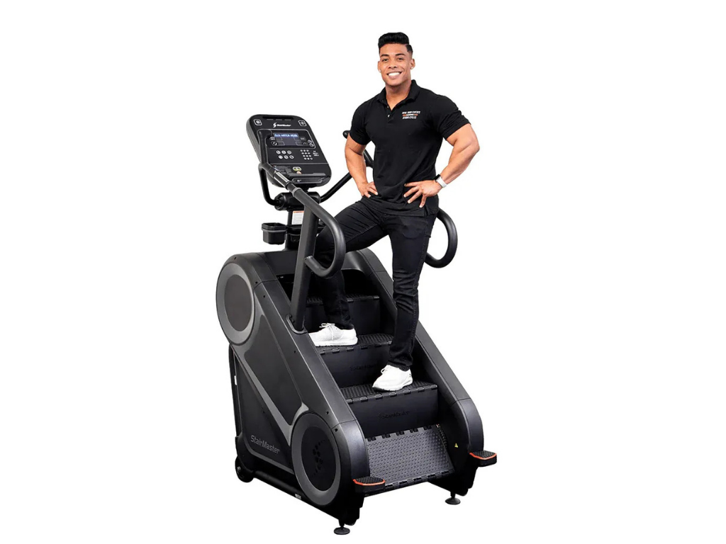 A smiling man in a black polo shirt stands on a stair climber machine.