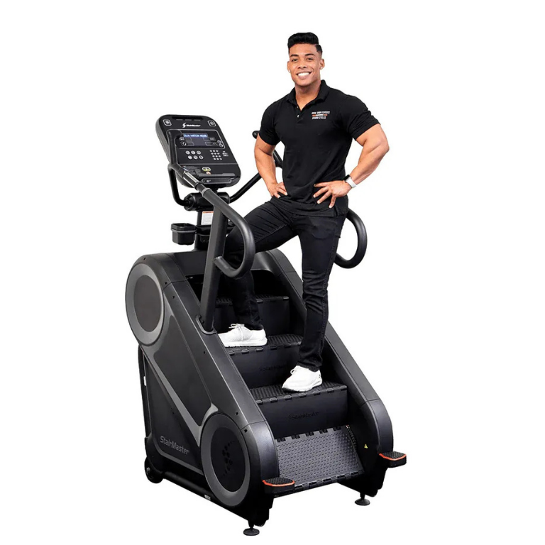 A smiling man in a black polo shirt stands on a stair climber machine.