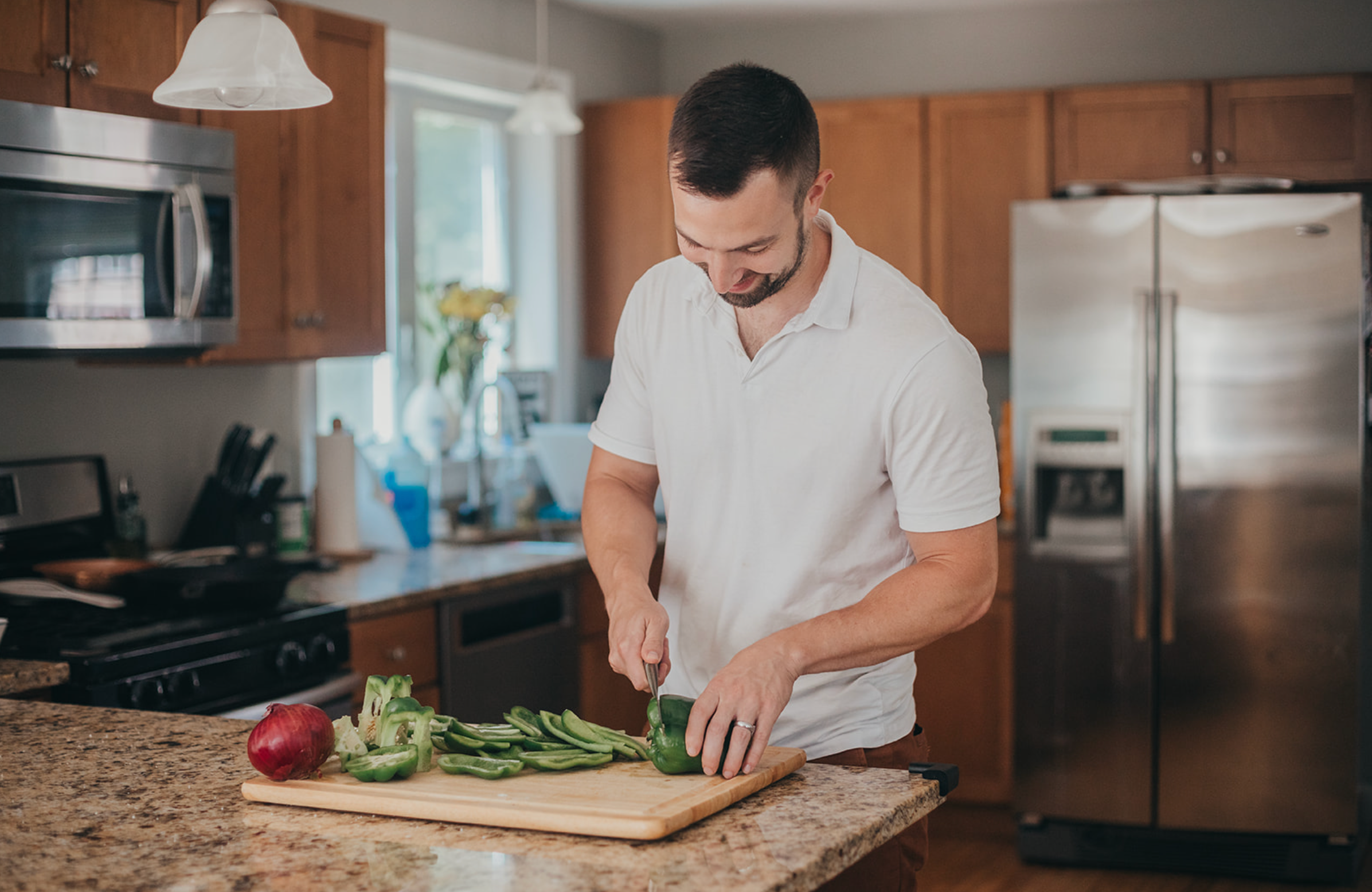 A man chops green bell peppers on a cutting board in a kitchen.