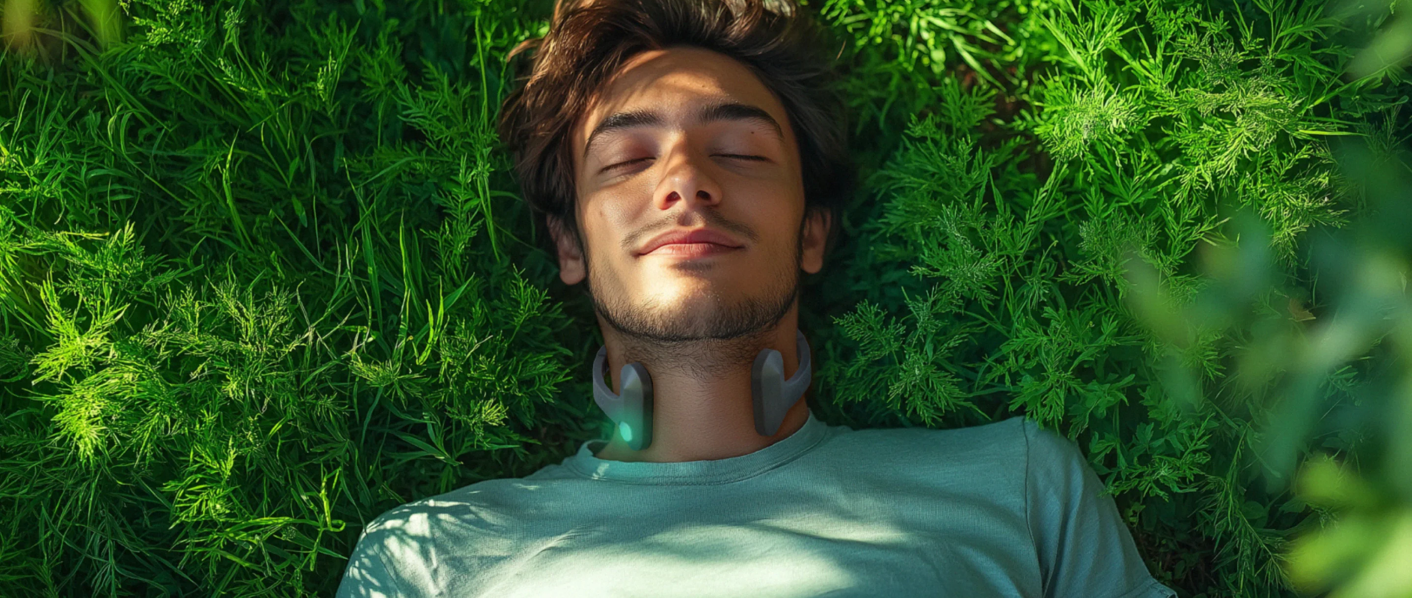 Man lying peacefully in lush green grass with eyes closed, wearing a Pulsetto device around his neck.