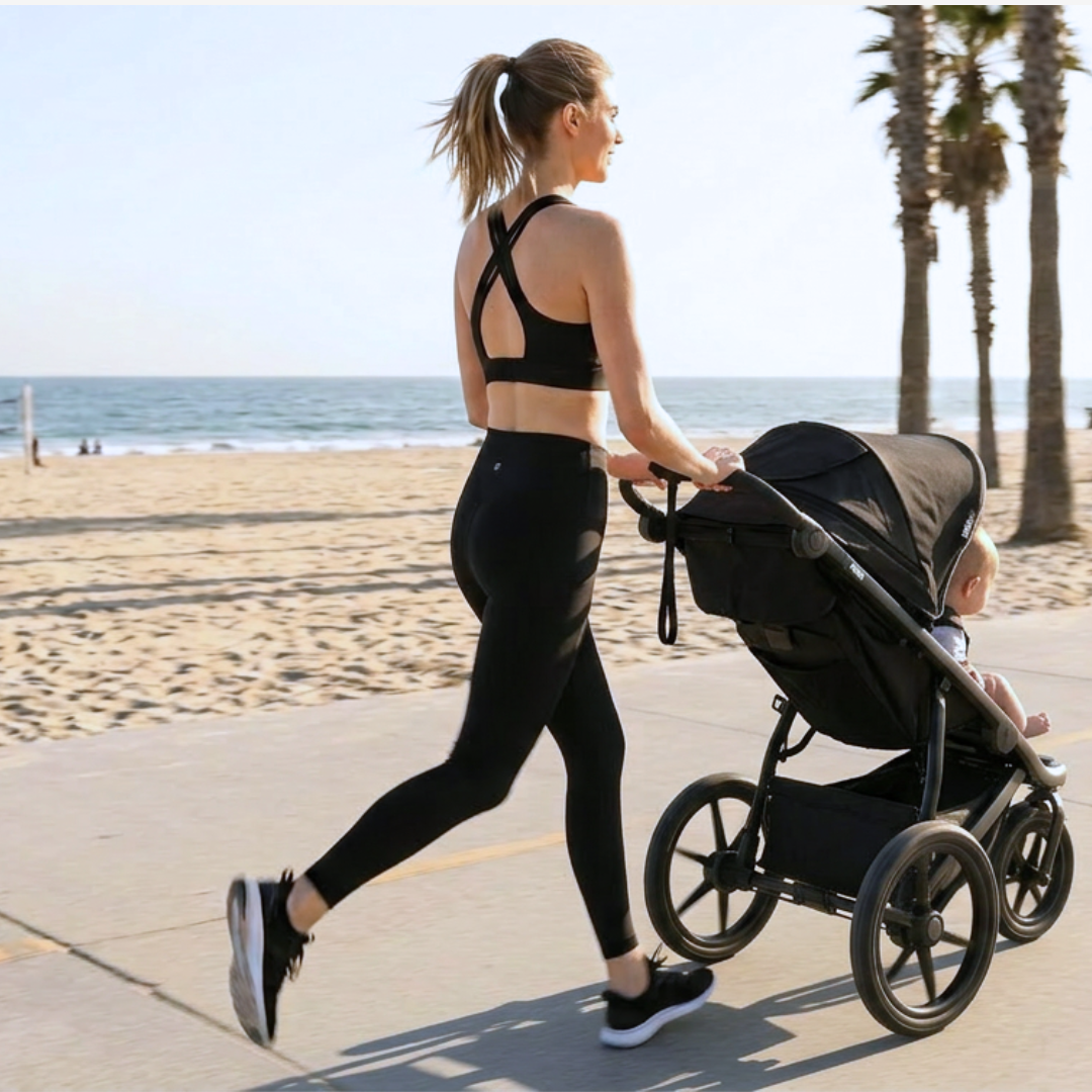 A woman runs along a beach path, pushing a baby in a stroller, with palm trees and the ocean behind her.