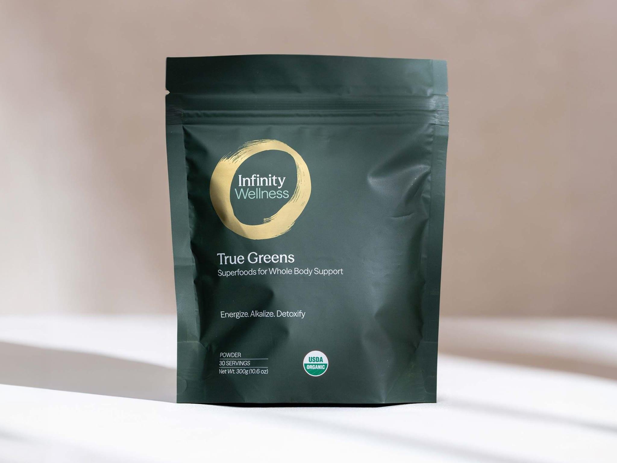 Dark green Infinity Wellness True Greens superfood powder pouch with a gold logo and USDA Organic seal.