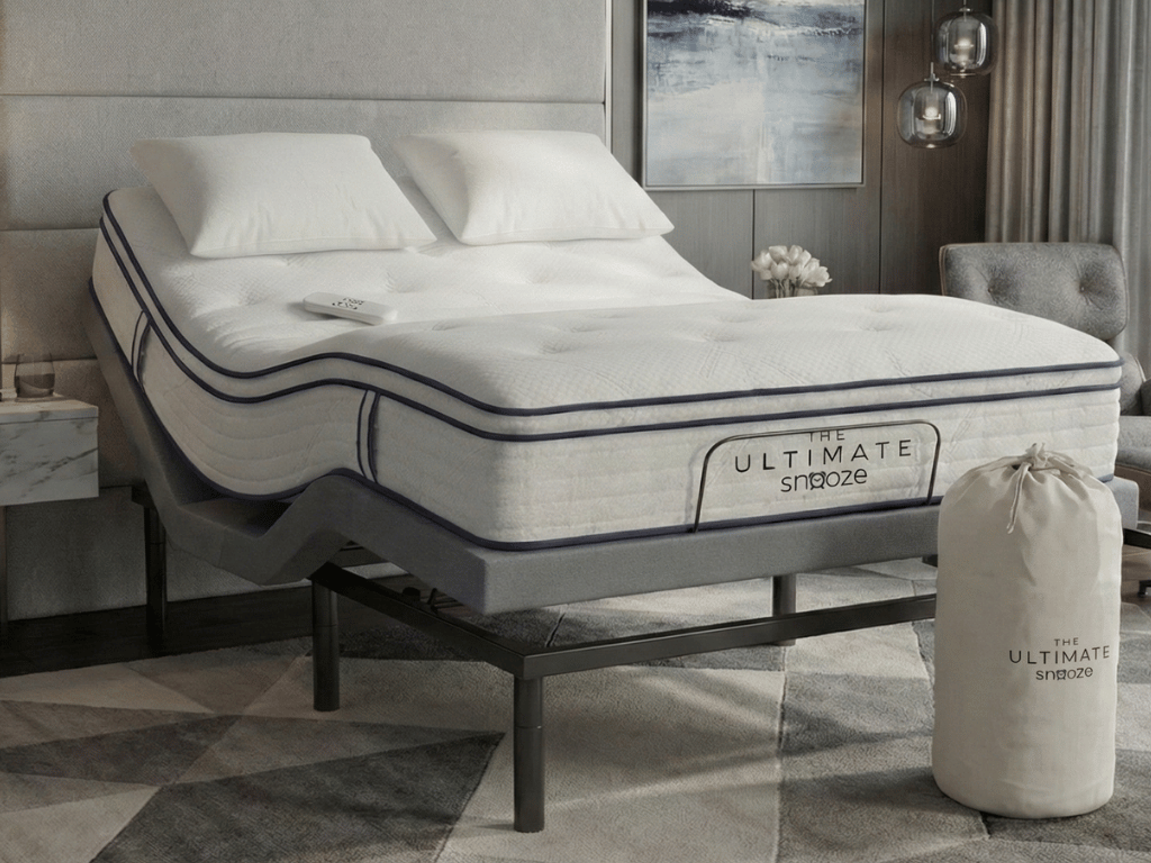 An adjustable bed featuring "The Ultimate Snooze" mattress, a remote, and a matching branded storage bag.