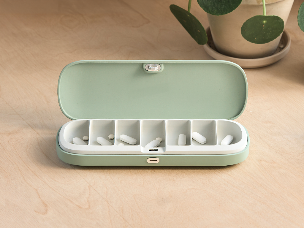 Open mint green pill organizer with white pills on a wooden surface.