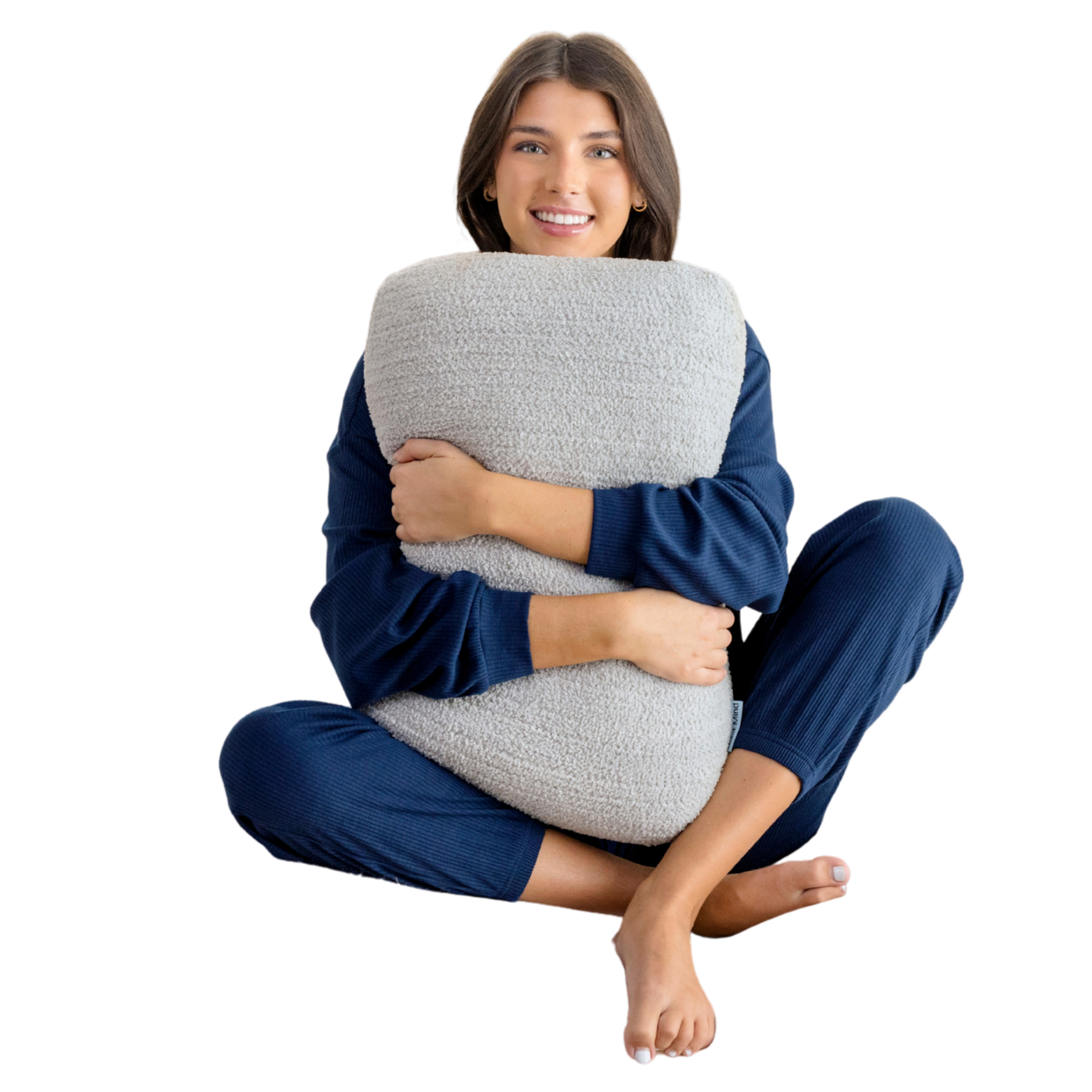 A smiling woman in blue loungewear sits cross-legged, hugging a textured grey pillow.