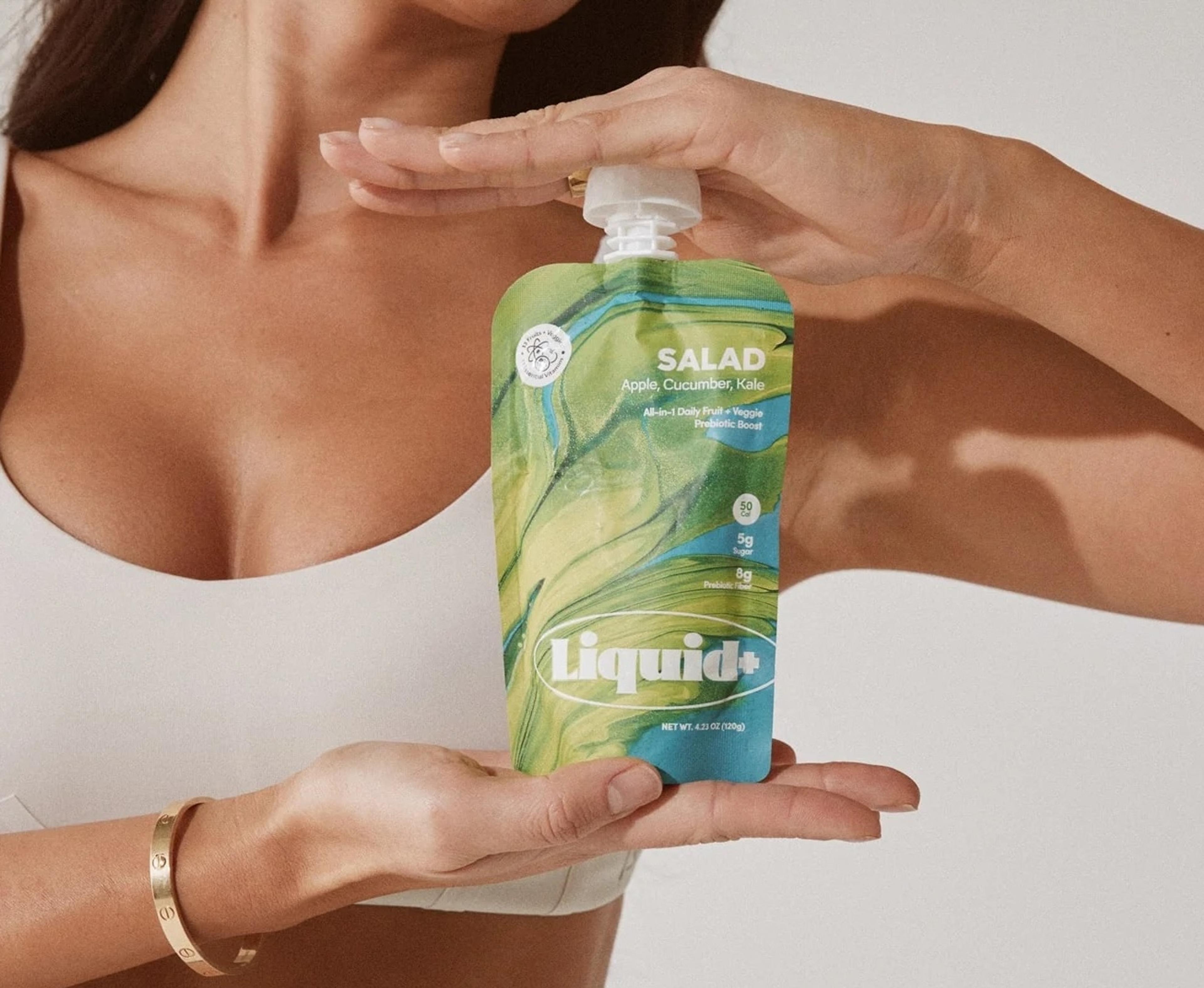 A woman holds a green and blue Liquid+ 'Salad' pouch.
