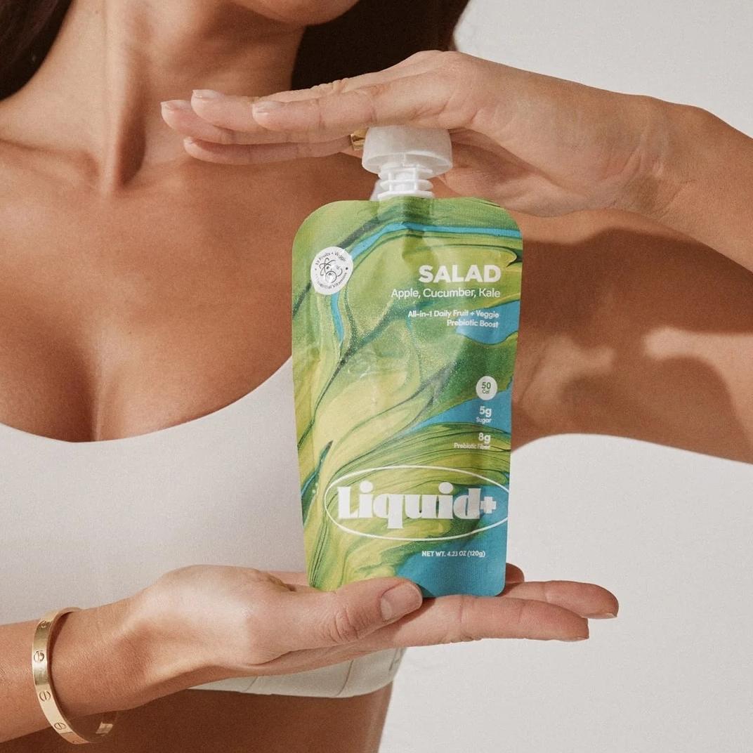 A woman holds a green and blue Liquid+ 'Salad' pouch.