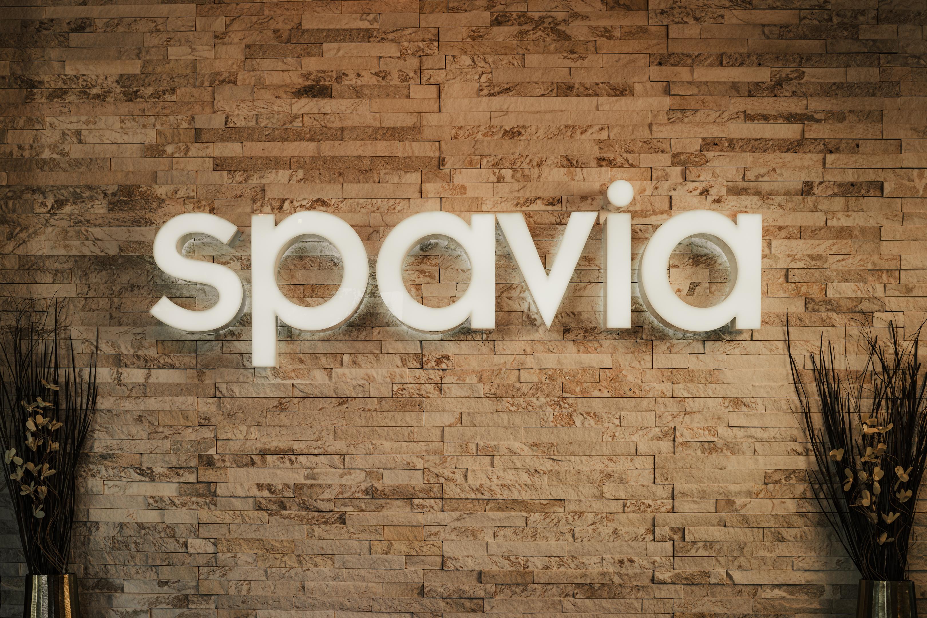 Illuminated "spavia" sign on a textured stone wall.