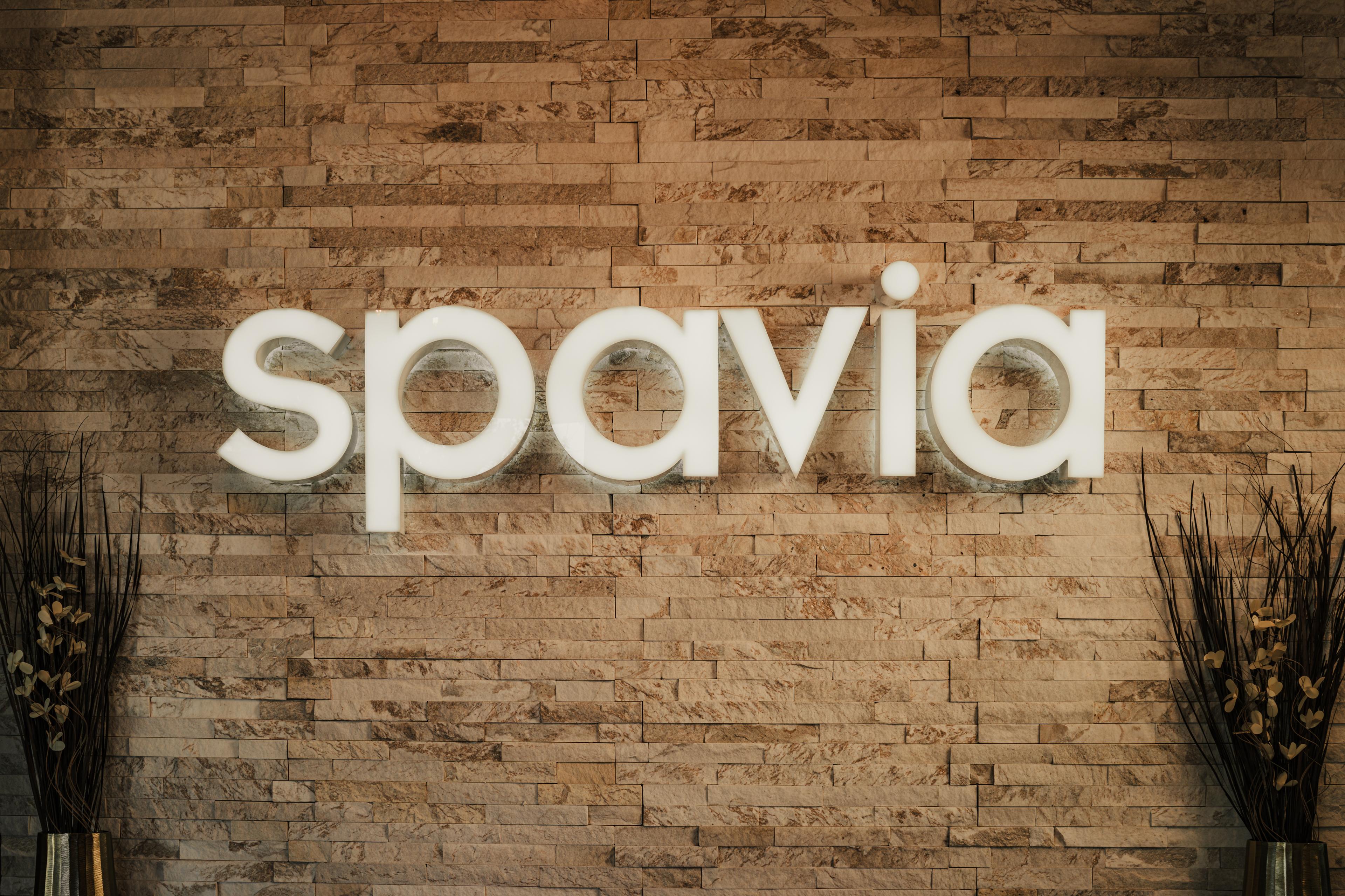 Illuminated "spavia" sign on a textured stone wall.