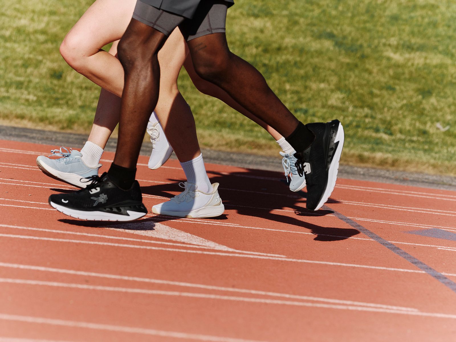 Three runners' legs and sneakers in stride on a red track.