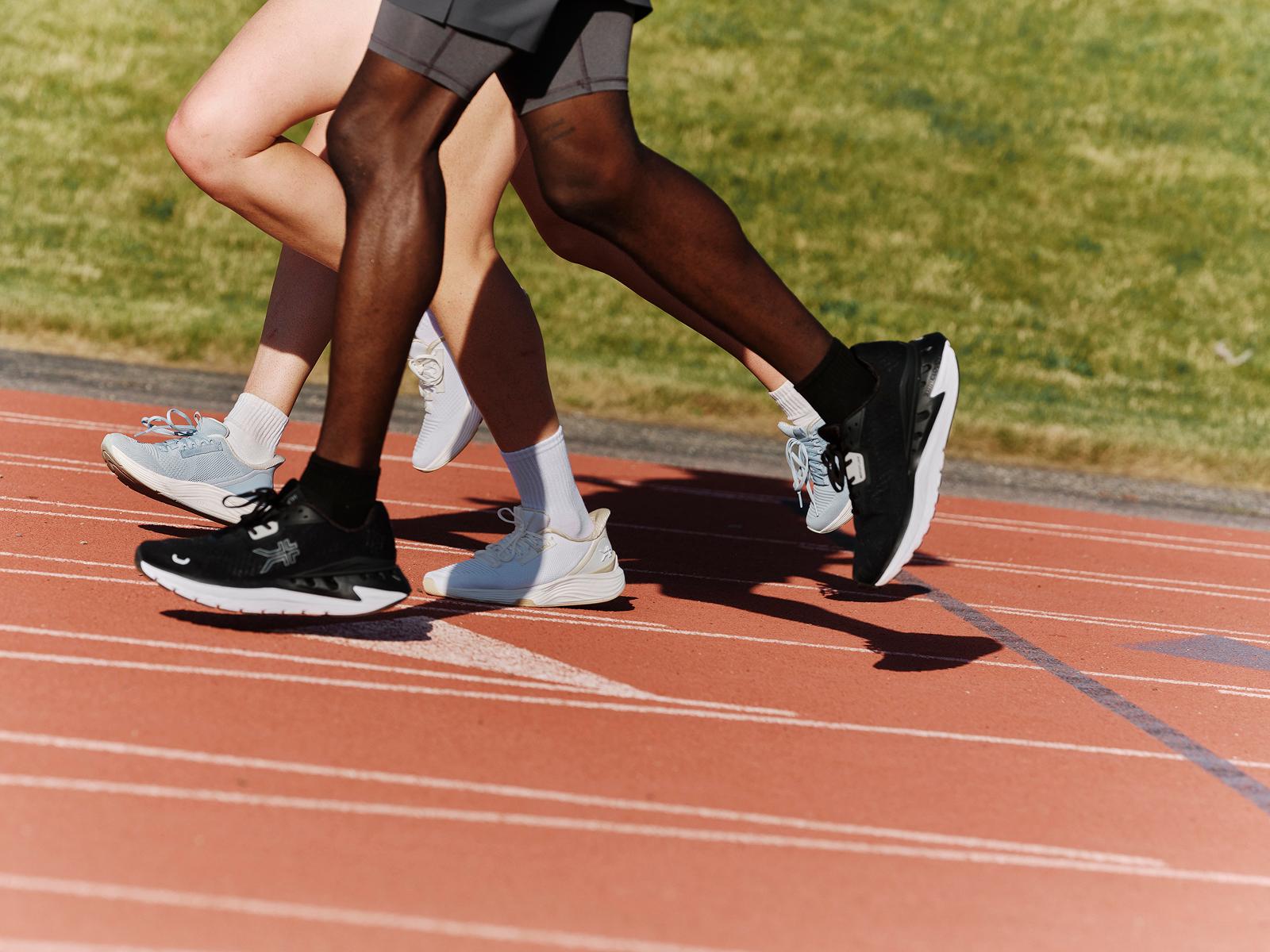 Three runners' legs and sneakers in stride on a red track.