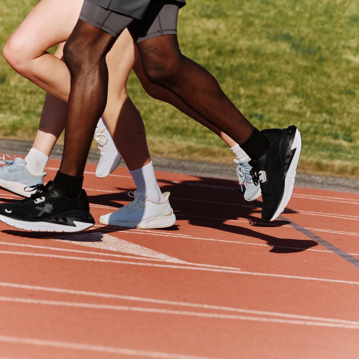 Three runners' legs and sneakers in stride on a red track.