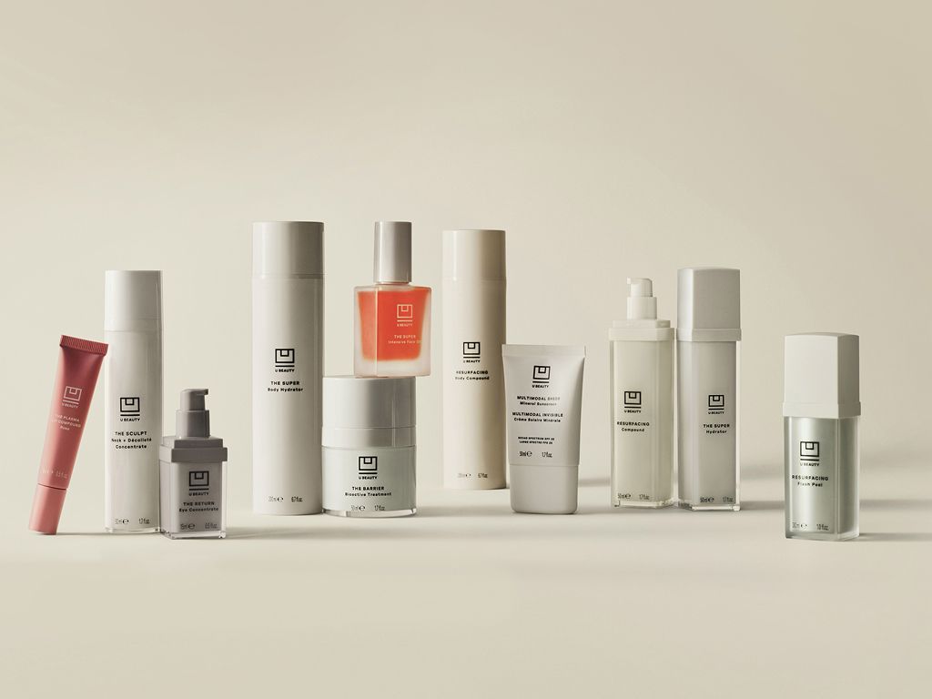 A collection of minimalist skincare products in various white, light, pink, orange, and silver bottles, tubes, and jars.