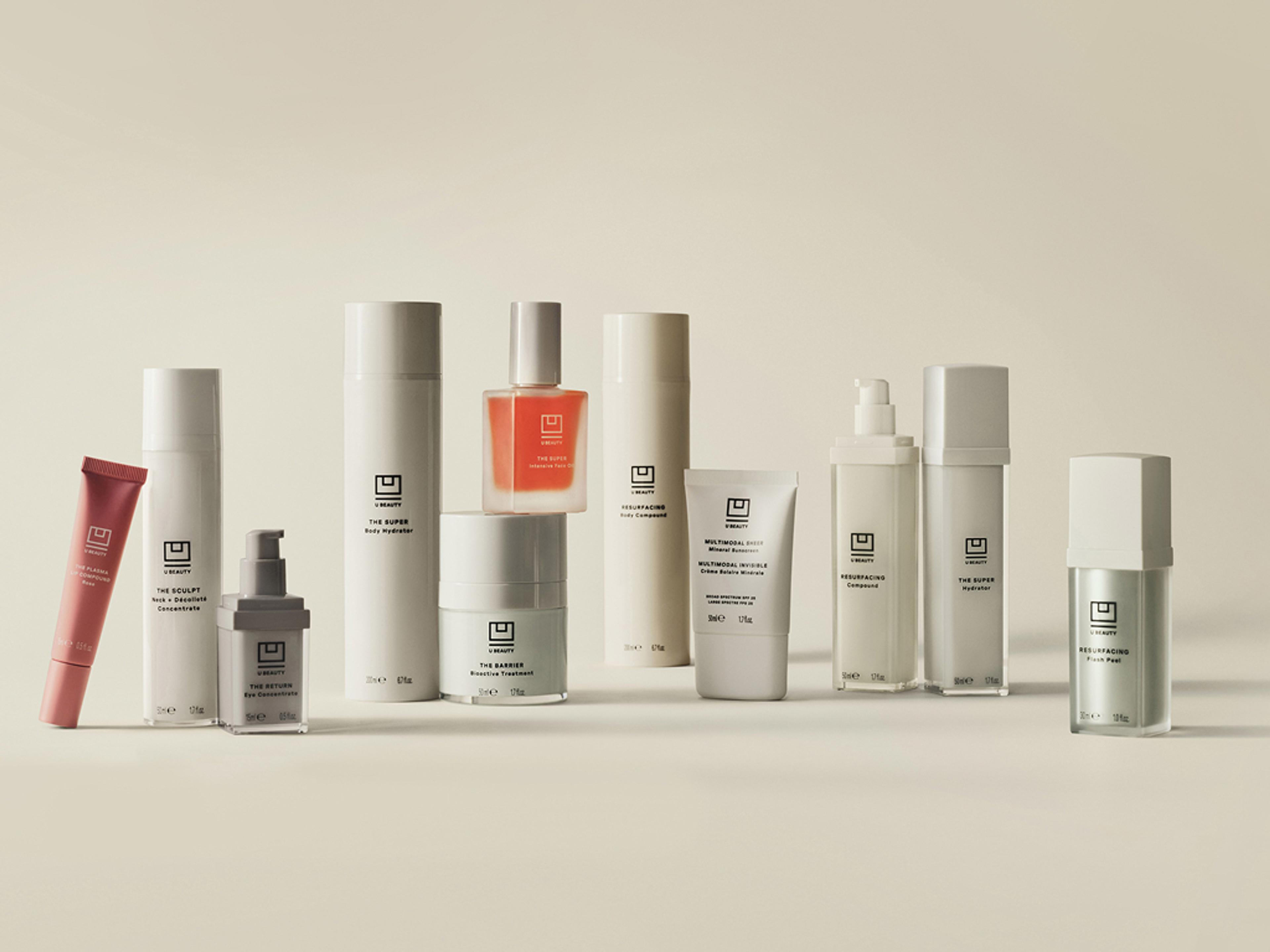 A collection of minimalist skincare products in various white, light, pink, orange, and silver bottles, tubes, and jars.