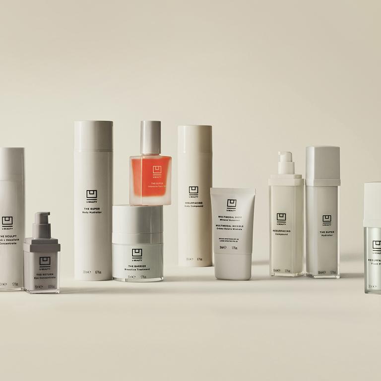 A collection of minimalist skincare products in various white, light, pink, orange, and silver bottles, tubes, and jars.