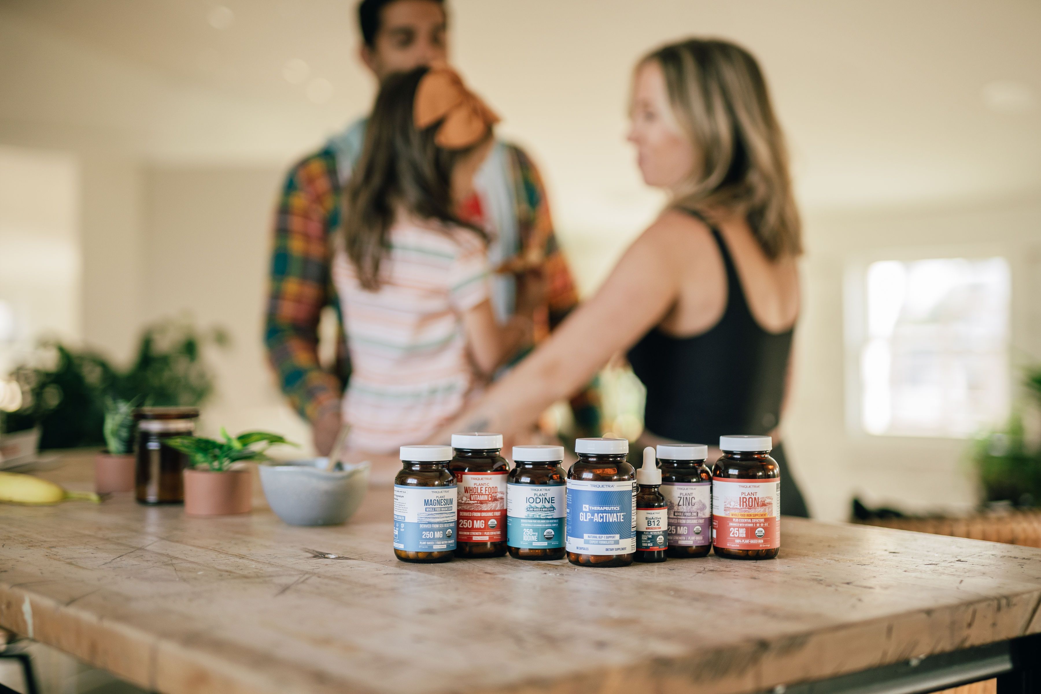 Several supplement bottles on a wooden table with a blurred family in the background.