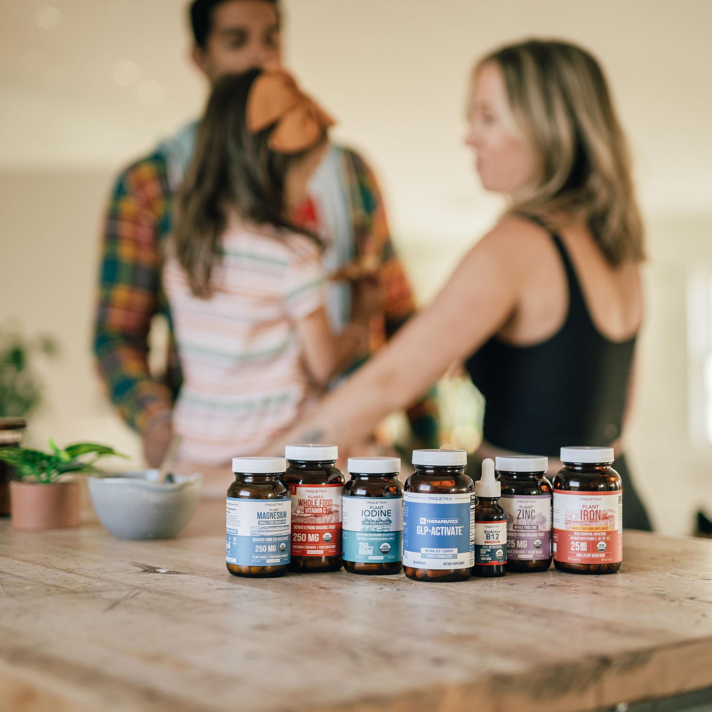 Several supplement bottles on a wooden table with a blurred family in the background.
