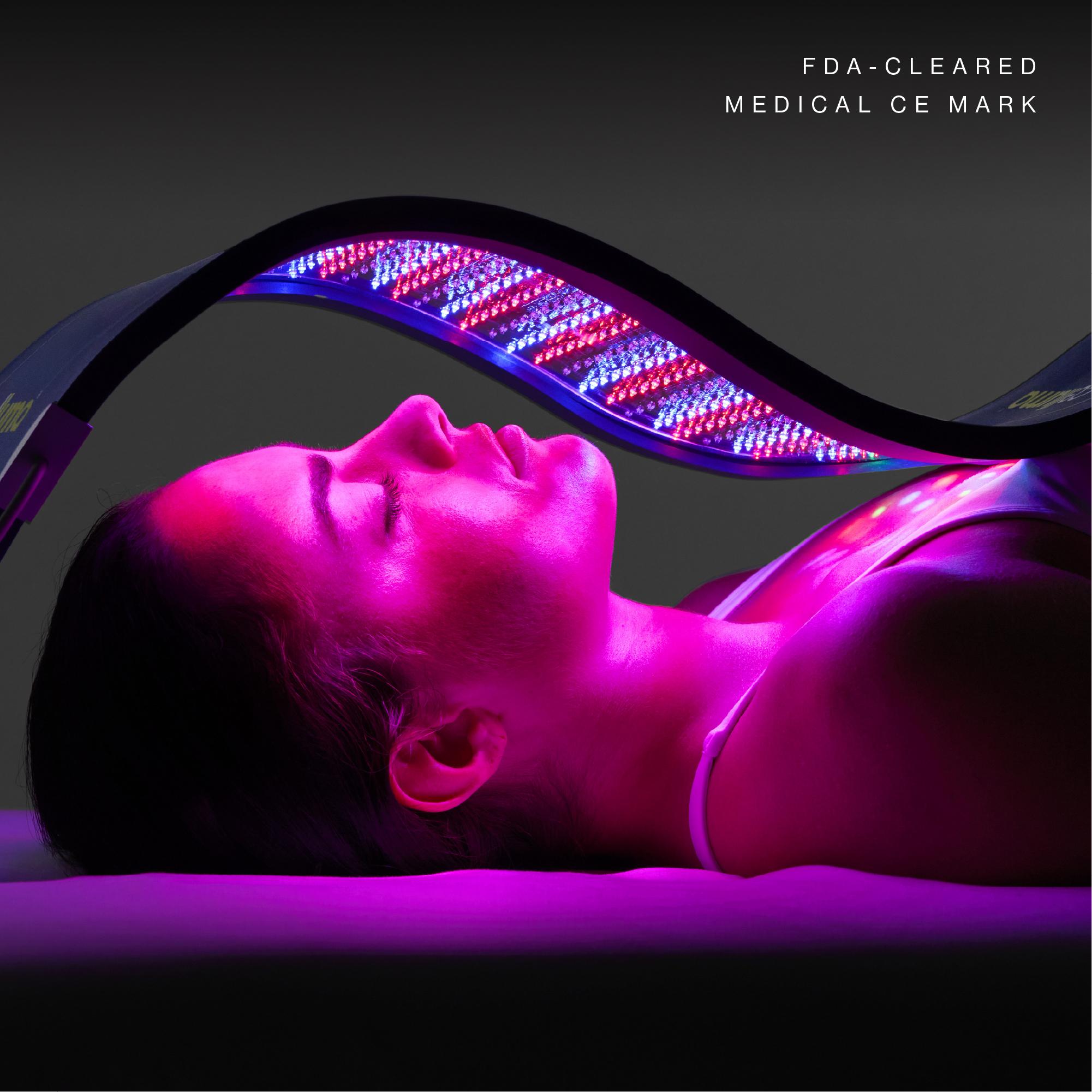 Woman receiving LED light therapy, illuminated by pink and purple light. Text: FDA-CLEARED MEDICAL CE MARK.