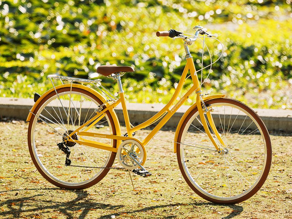 A bright yellow cruiser bike with brown tires and saddle, parked on sunny grass.