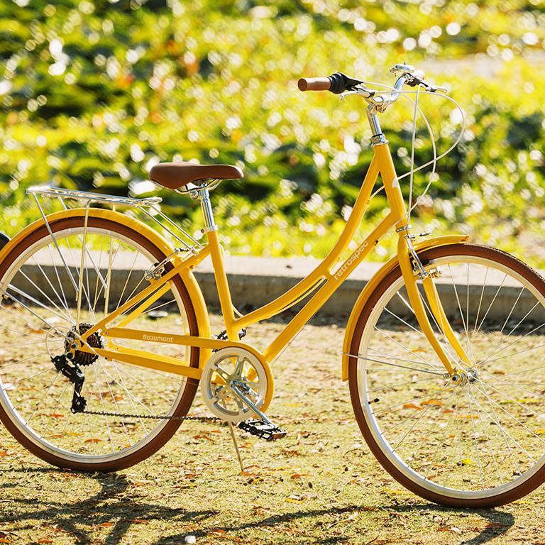 A bright yellow cruiser bike with brown tires and saddle, parked on sunny grass.