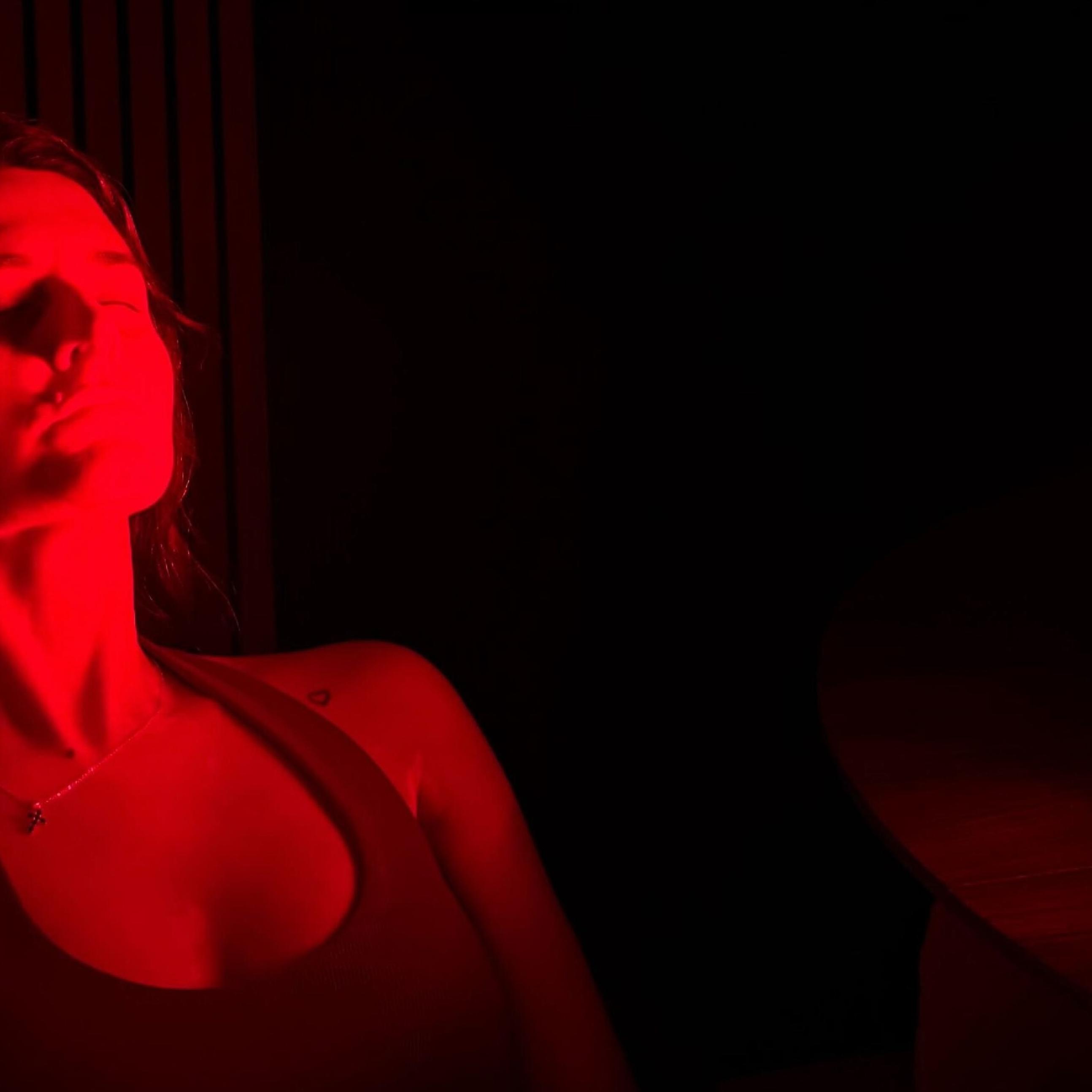 A woman with her eyes closed, illuminated by red light from a therapy panel.