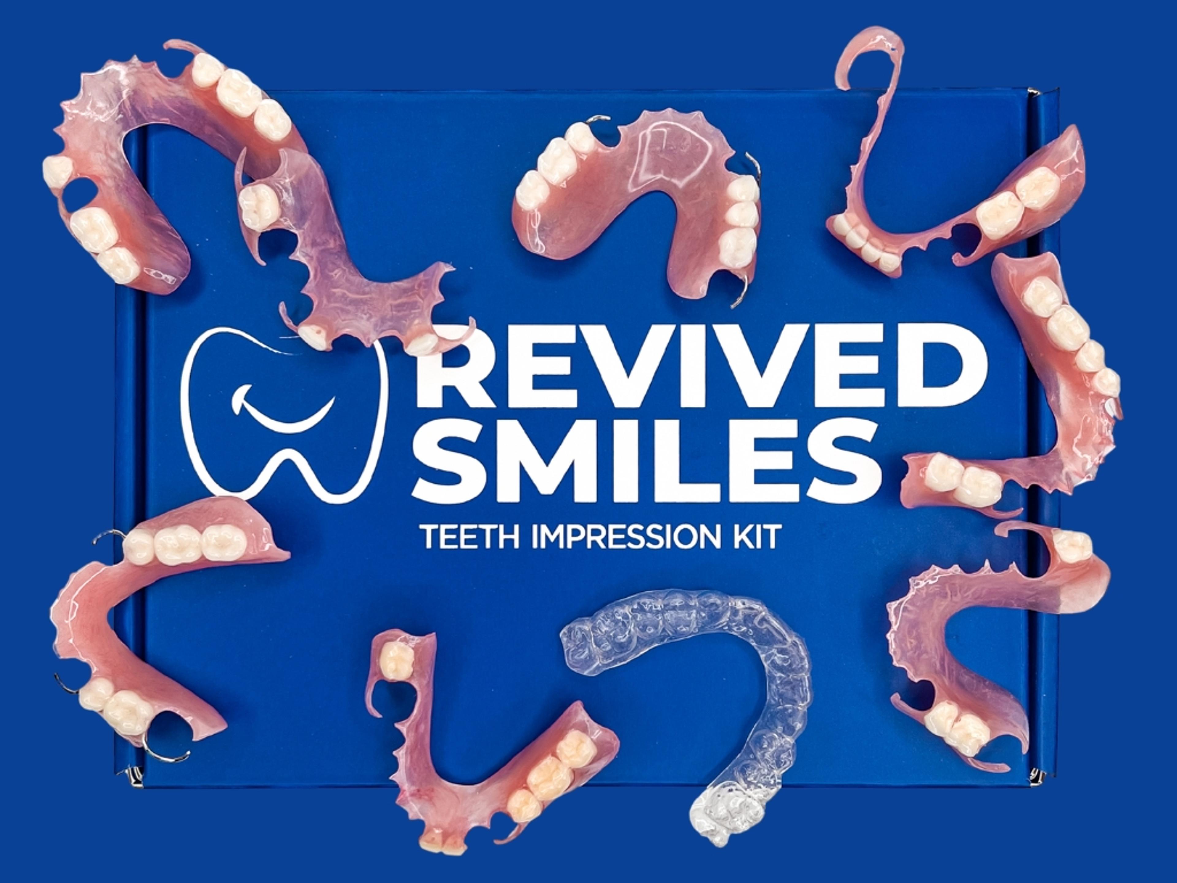 An overhead view of a blue "REVIVED SMILES TEETH IMPRESSION KIT" box, featuring a tooth logo, surrounded by several pink partial dentures and a clear dental aligner.
