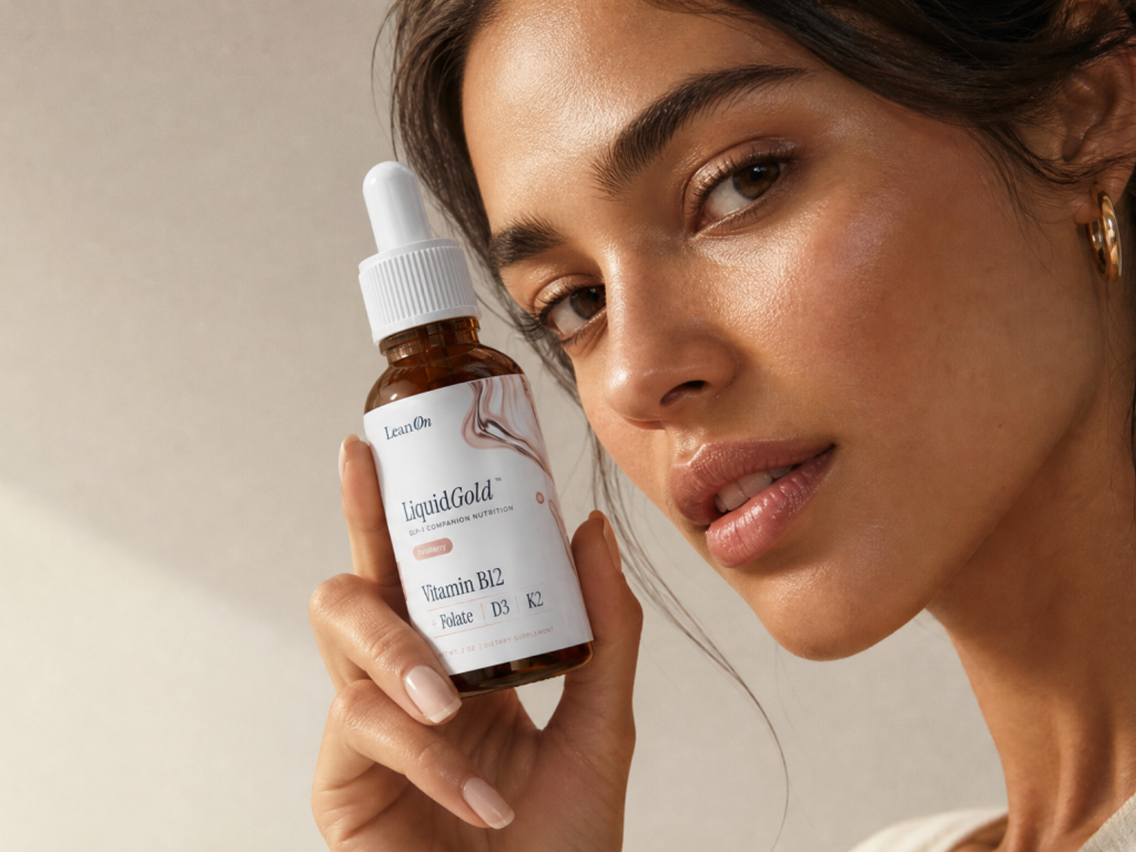 Close-up of a woman with glowing skin holding a bottle of LiquidGold Vitamin B12 supplement.