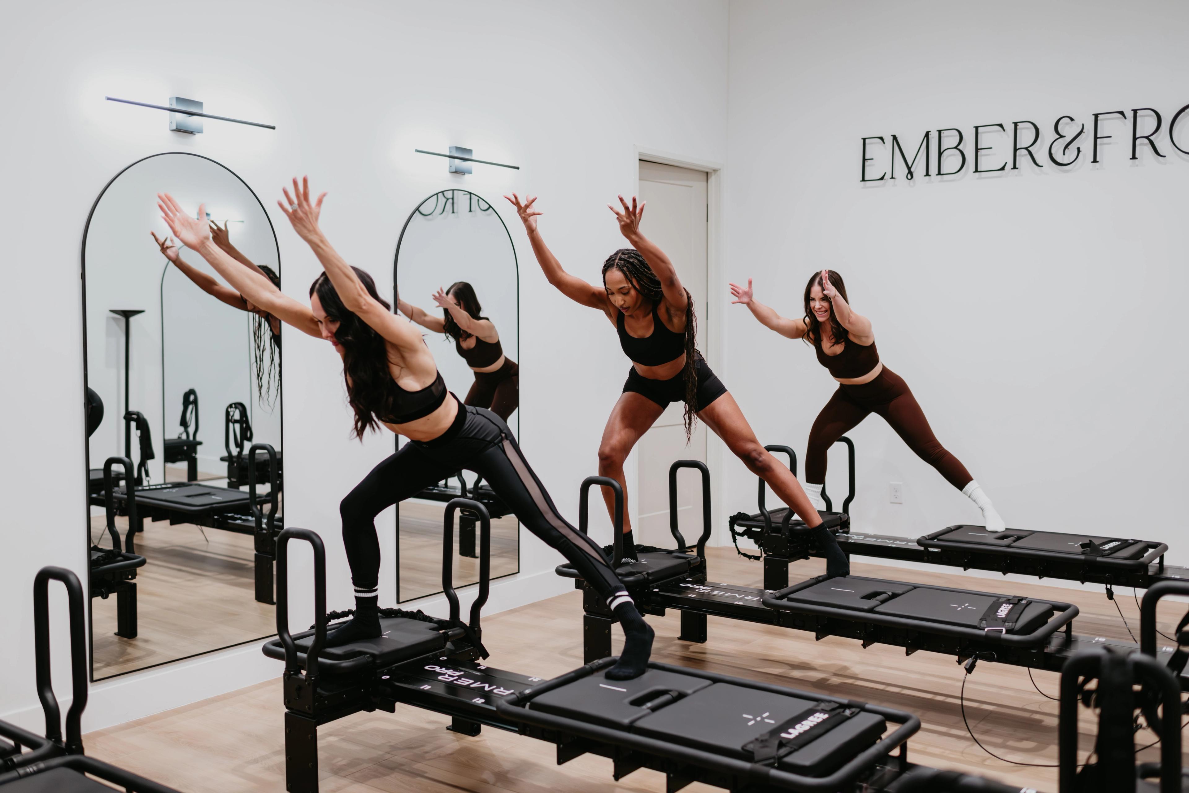 Three women exercising on reformer machines in a modern fitness studio.