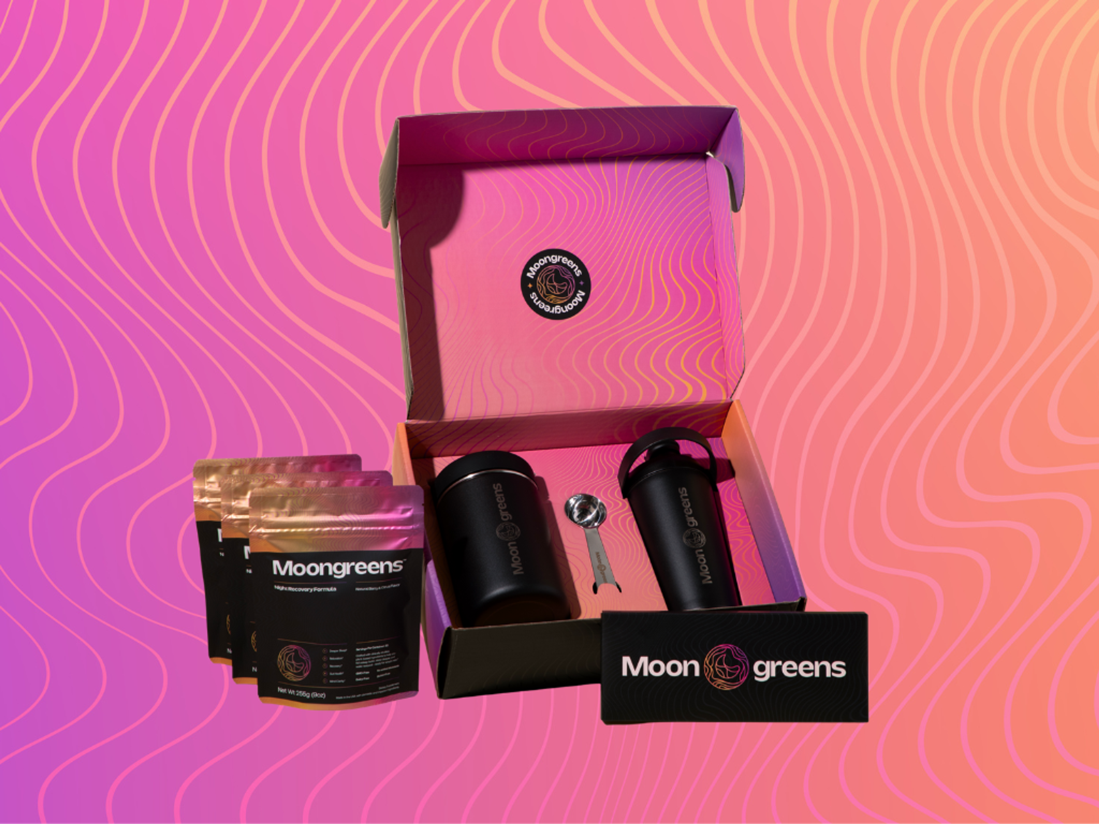 Moongreens branded gift set with a pink box, black tumbler, shaker bottle, spoon, and three supplement pouches.