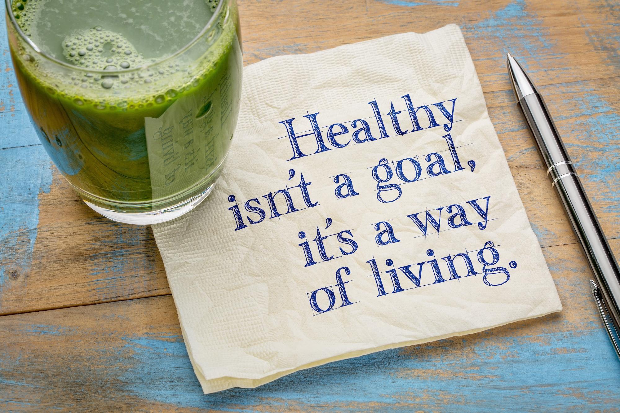 Green smoothie next to a napkin with the quote: "Healthy isn't a goal, it's a way of living."