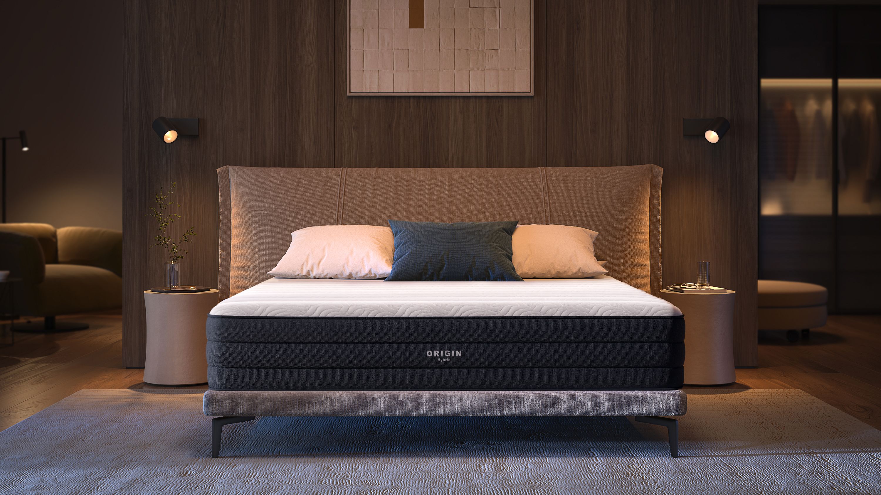 A black and white Origin mattress on a bed in a modern, warmly lit bedroom with a beige headboard and bedside tables.