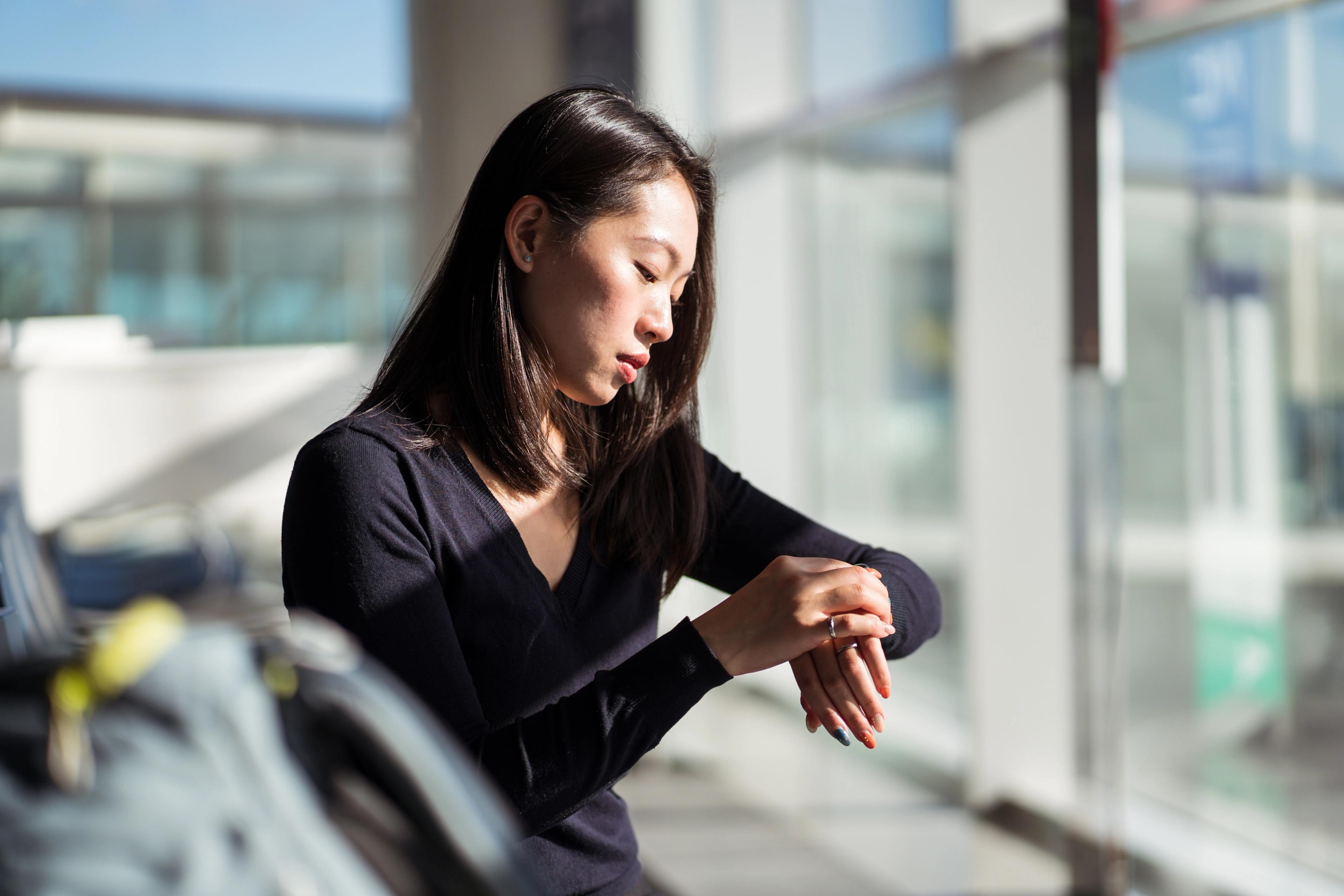 A woman checking the fitness tracker on her wrist while standing near a bright window