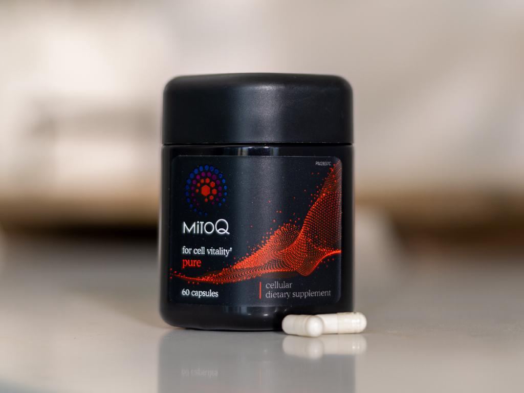 A black bottle of MitoQ Pure cellular dietary supplement with two white capsules in front.