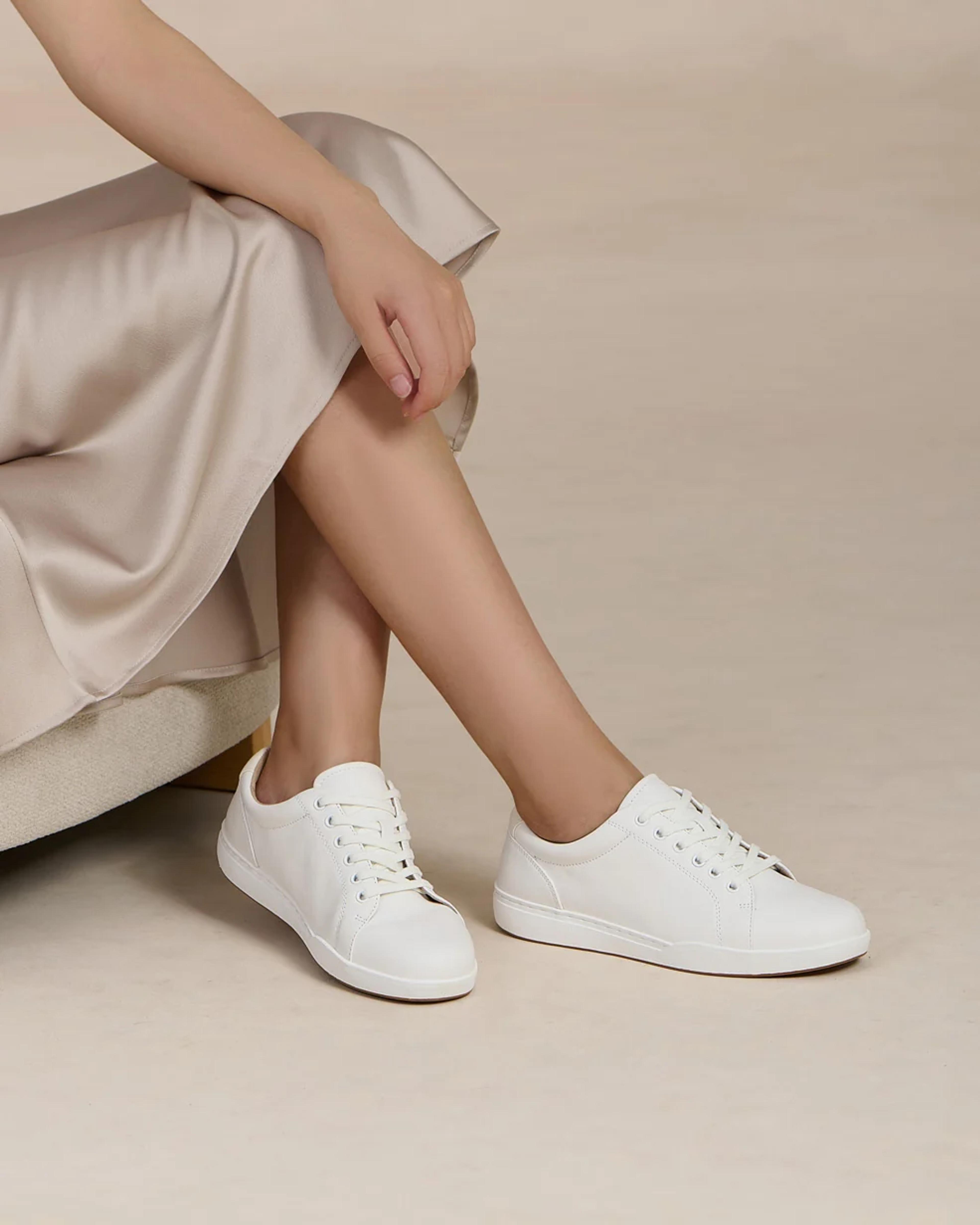 A person wearing a light-colored dress and white lace-up sneakers.