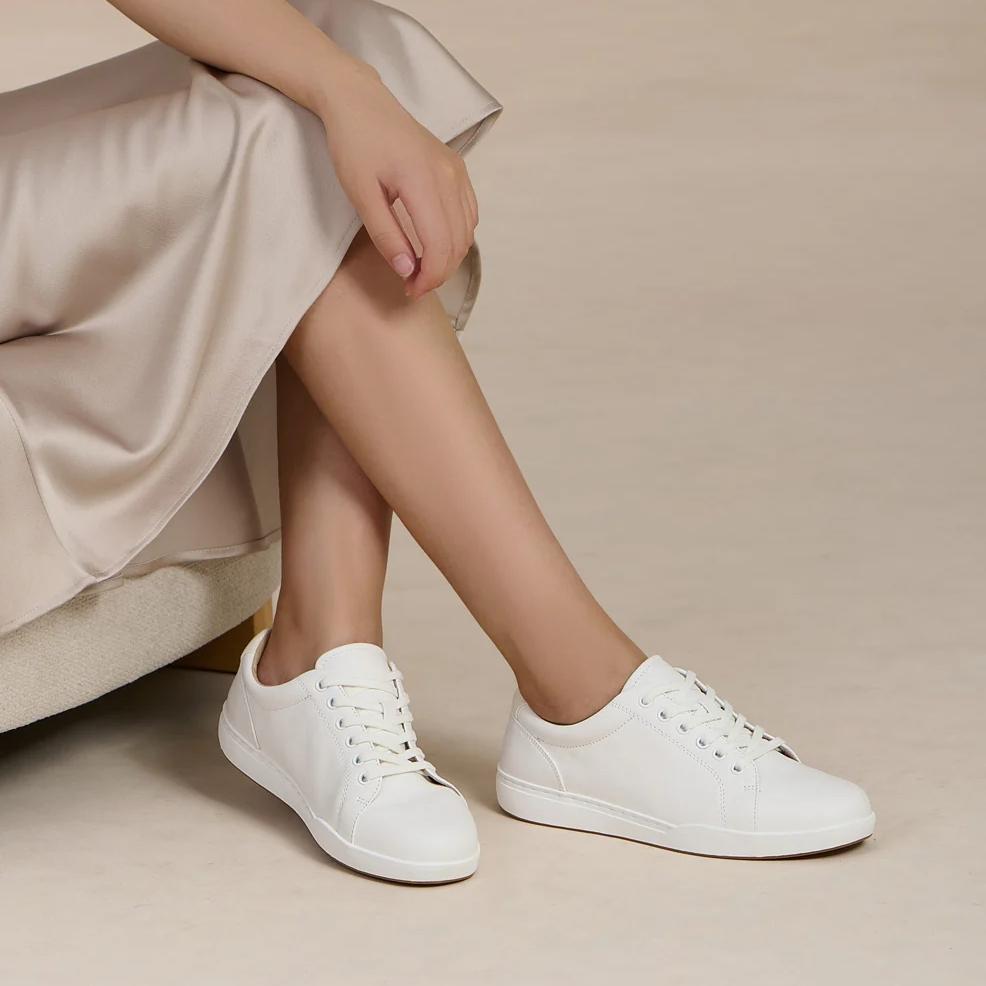 A person wearing a light-colored dress and white lace-up sneakers.