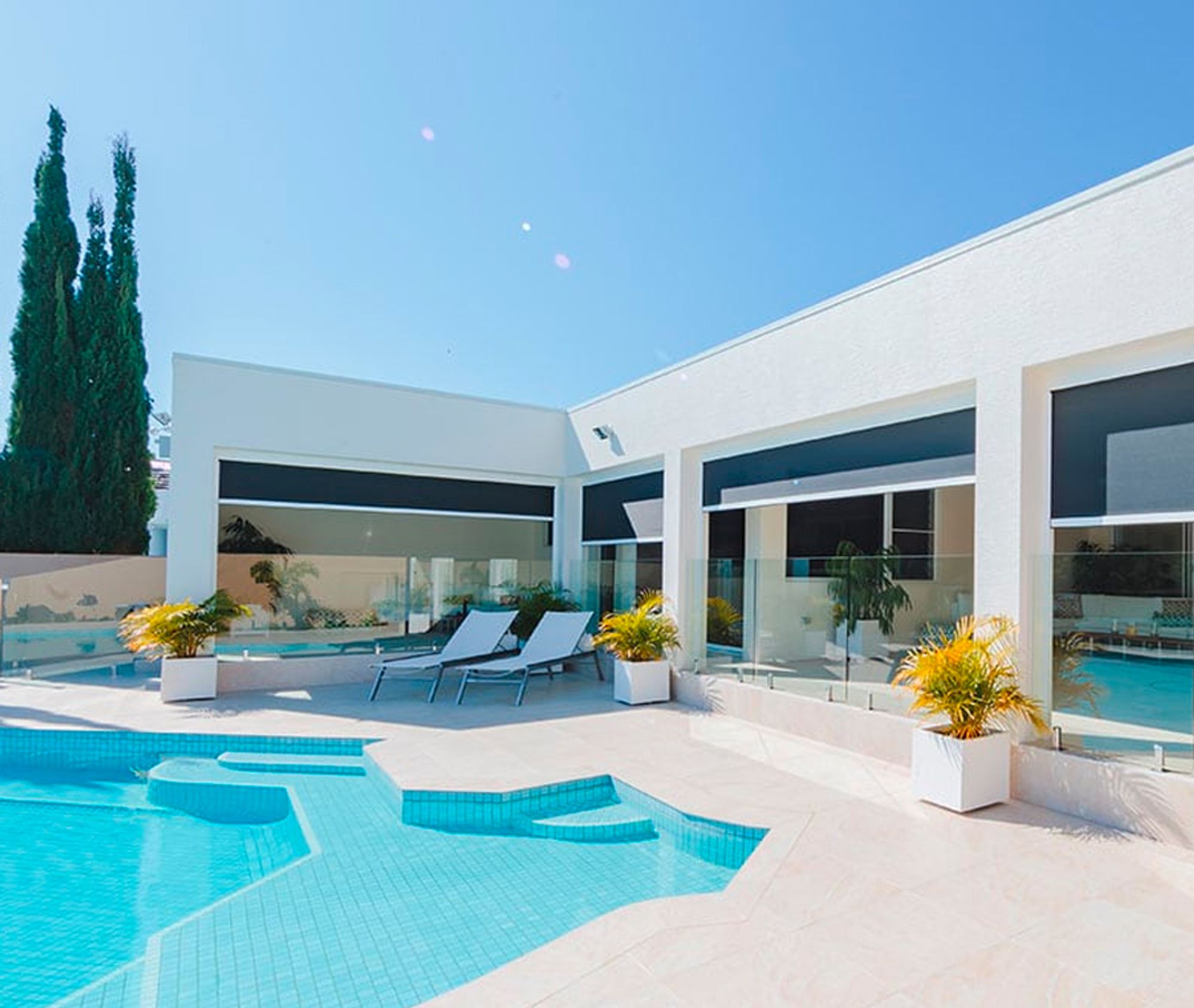 Outdoor blinds shading the alfresco windows of a white poolside home