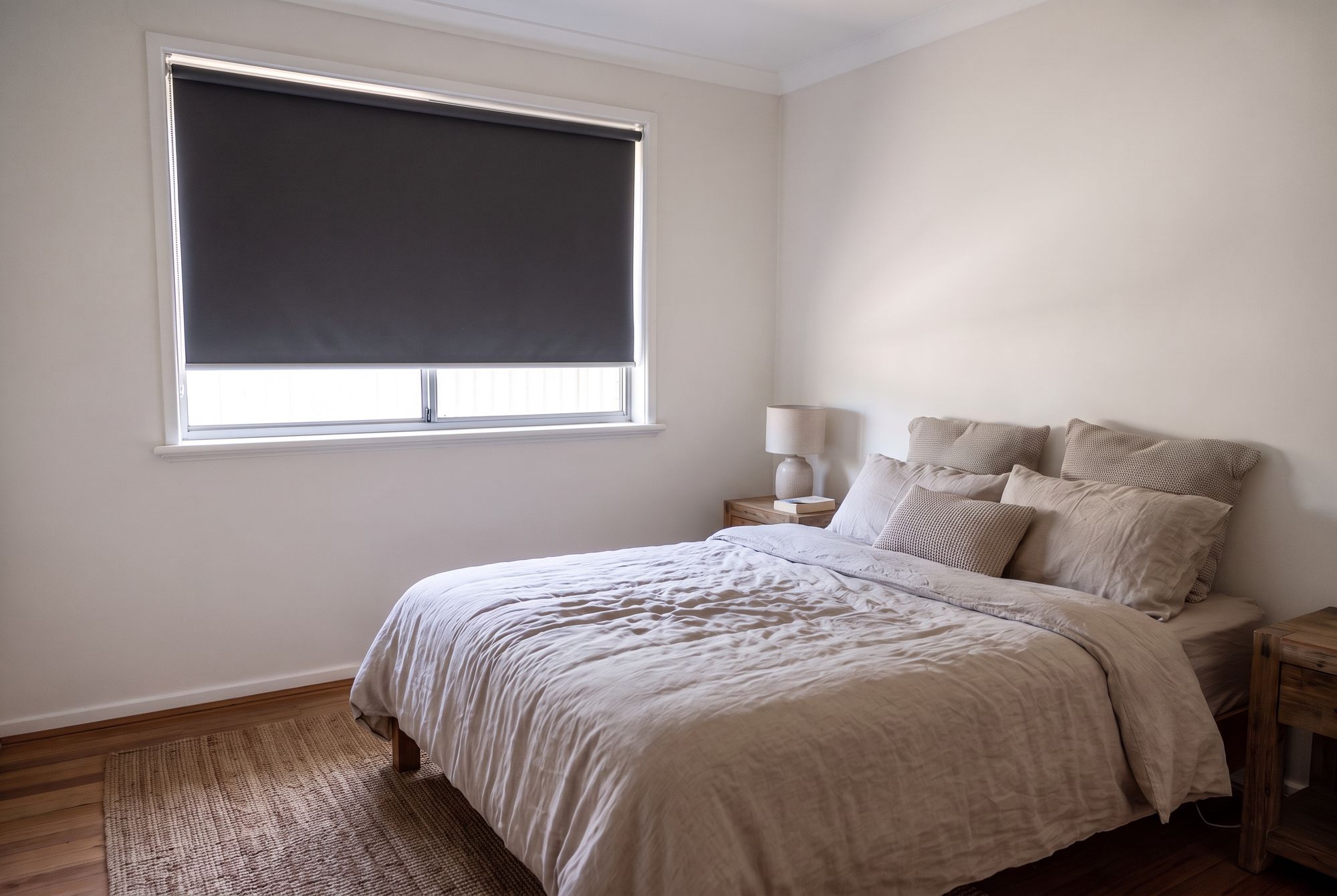 Bedroom with a charcoal blockout roller blind over the window and linen bedding