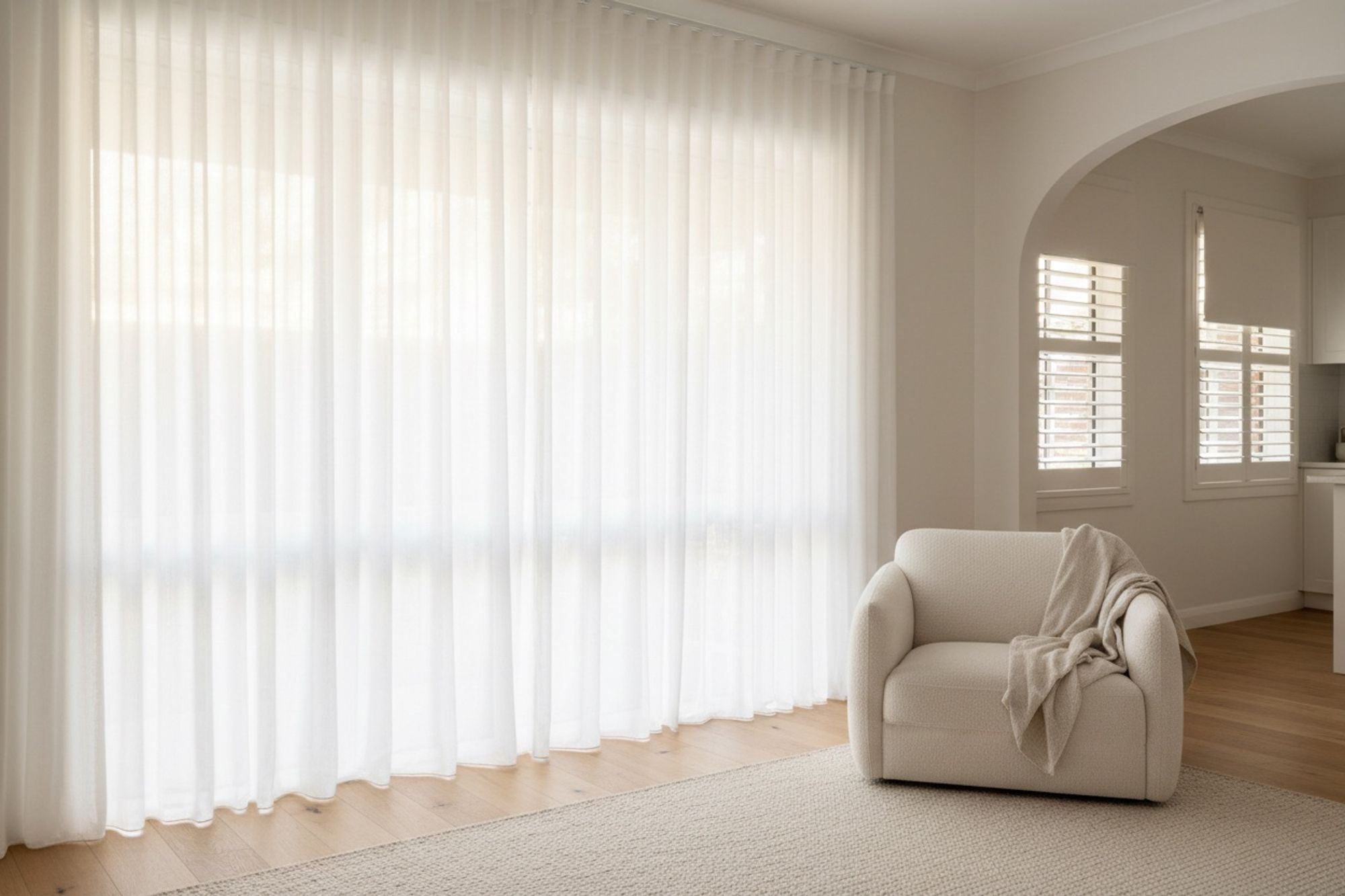White sheer wave-fold curtains, white plantation shutters and a white roller blind in a bright Perth living room