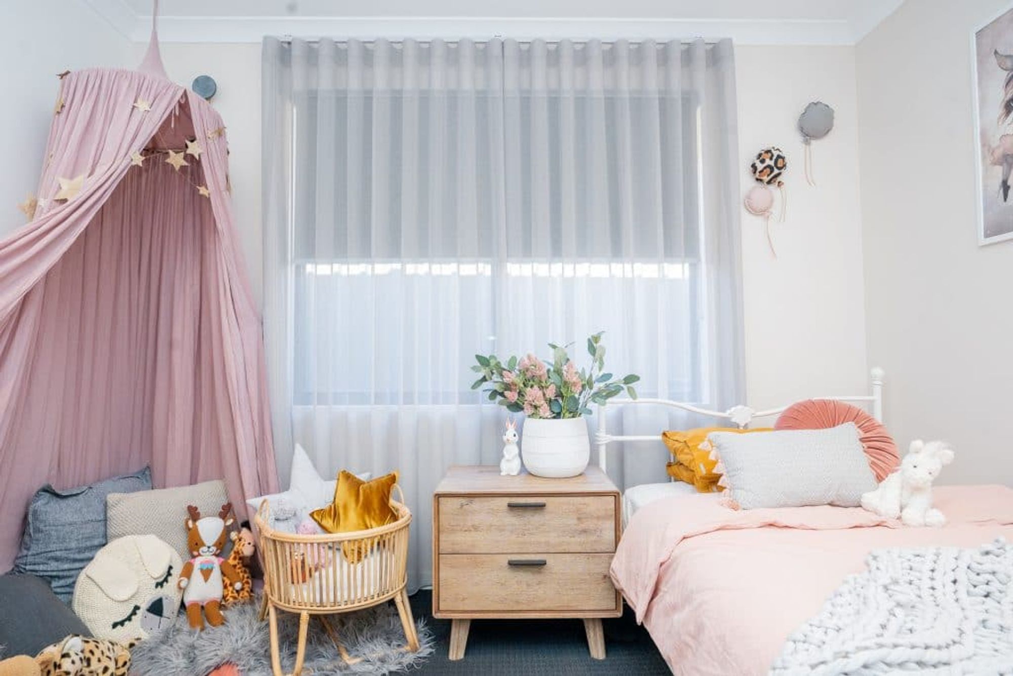 A child's bedroom with sheer curtains layered over a blind, beside a pink canopy bed