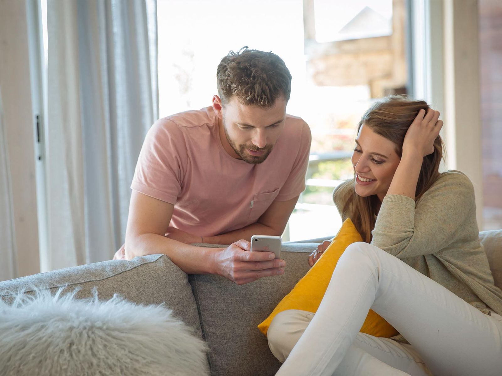 Couple adjusting motorised blinds from a phone in a bright, sunlit Perth living room