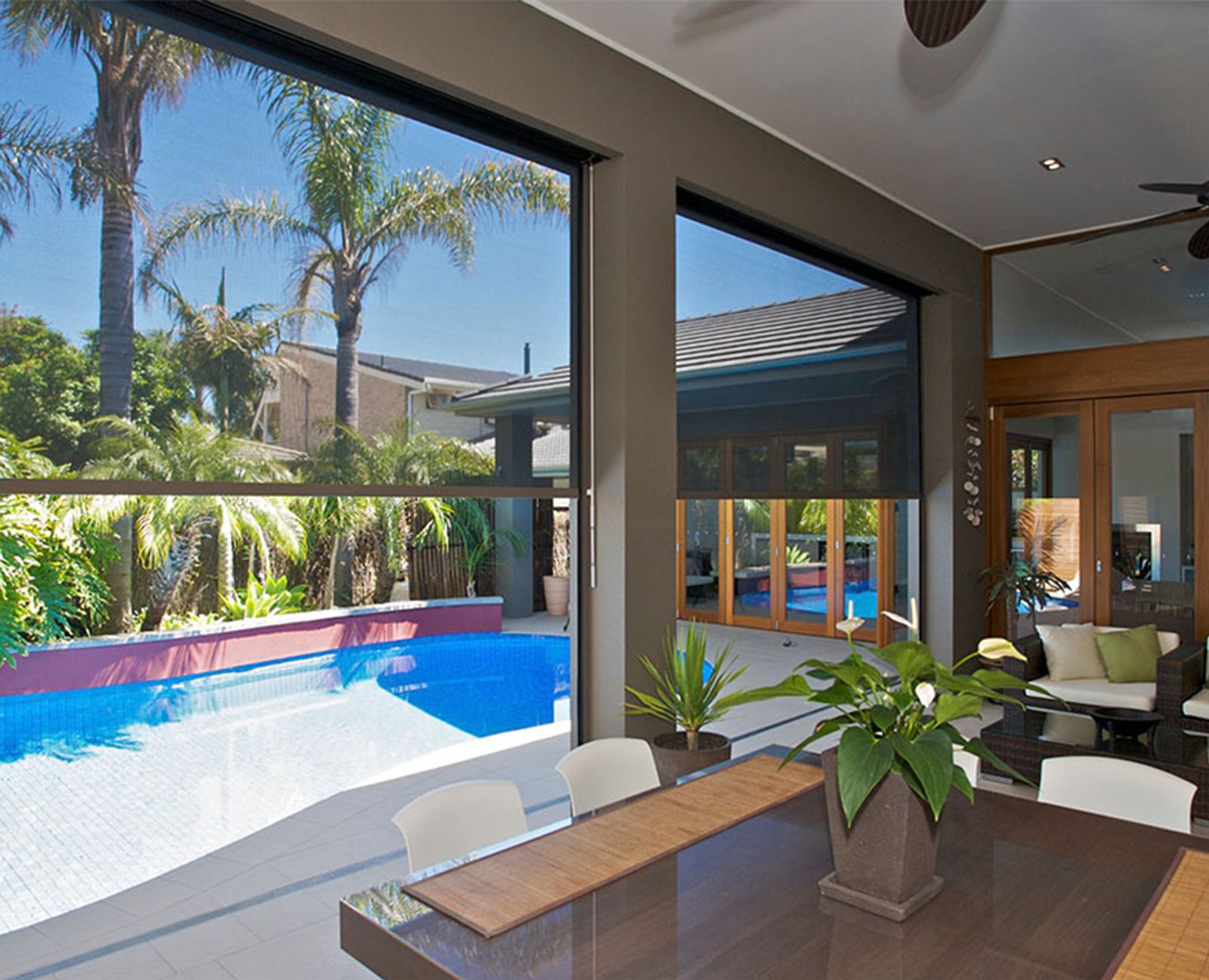 Outdoor blinds partly lowered between an alfresco dining area and the pool