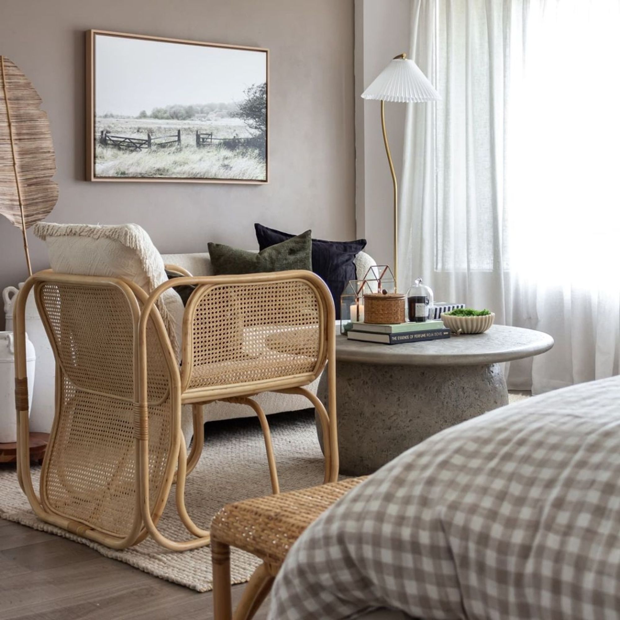 A neutral living room with white sheer curtains behind a rattan armchair