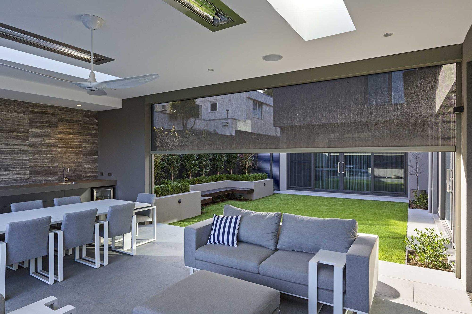Outdoor blinds lowered around a covered alfresco lounge and dining area overlooking a lawn