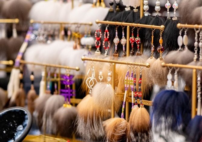 Handmade earrings with glass beads and furs of different colors and types hang on jewelry displays