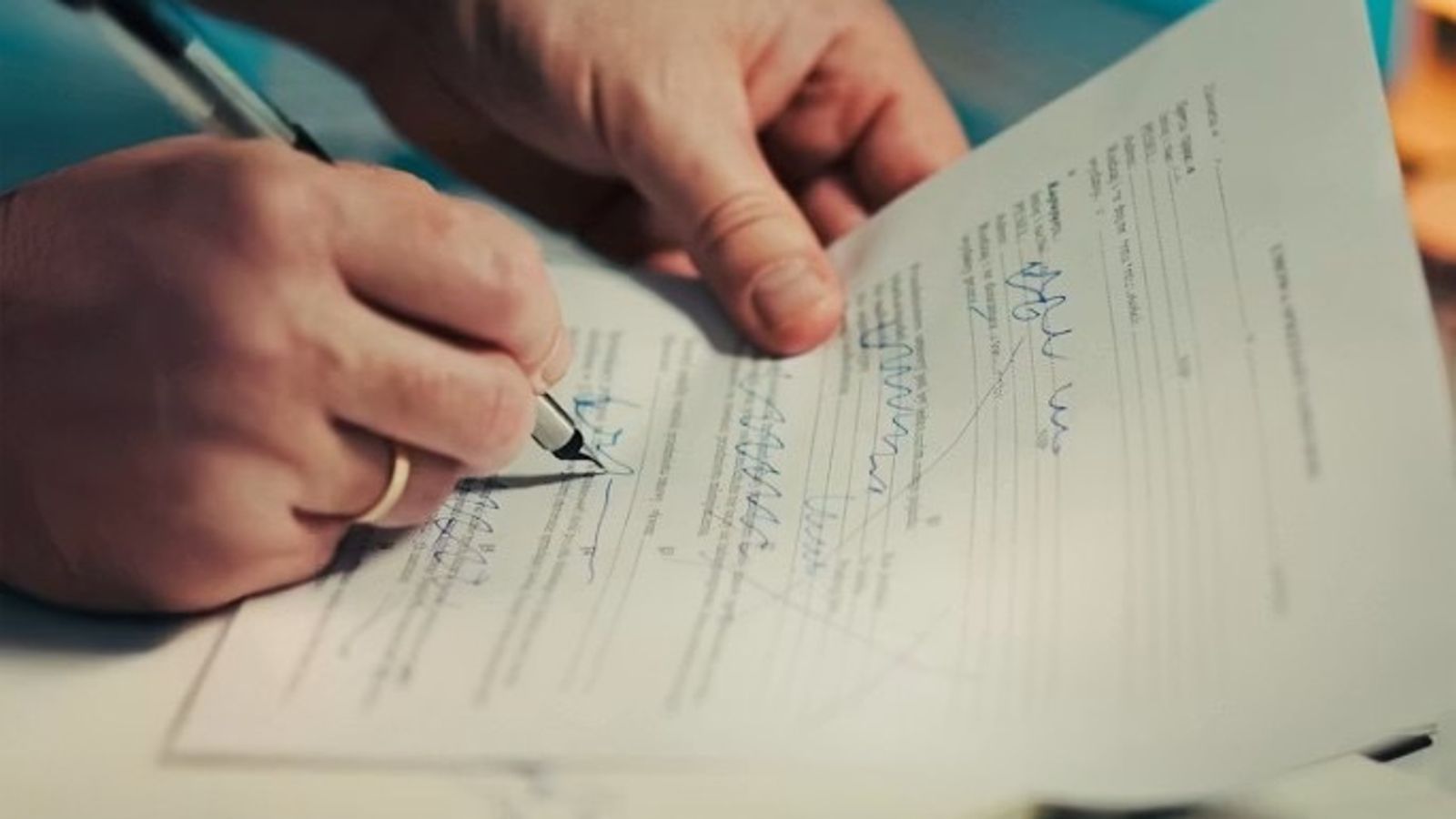 Close-up of hands signing a business document with a pen on a desk