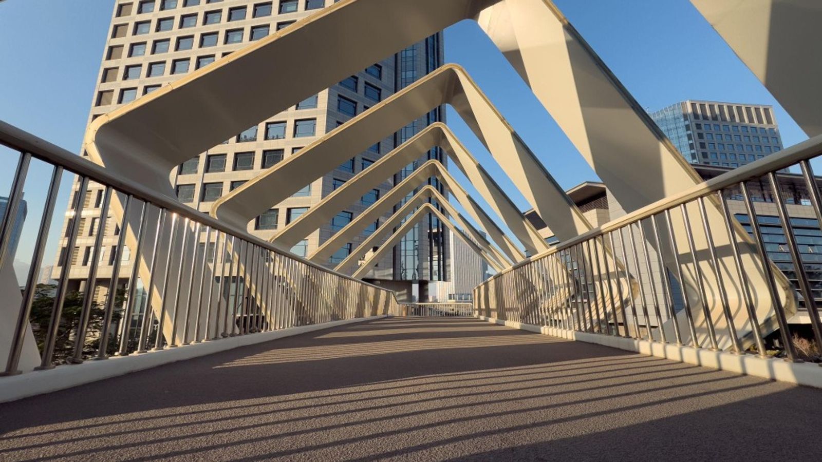 A modern pedestrian bridge with repeating white arches receding into the distance, suggesting consistency and forward movement