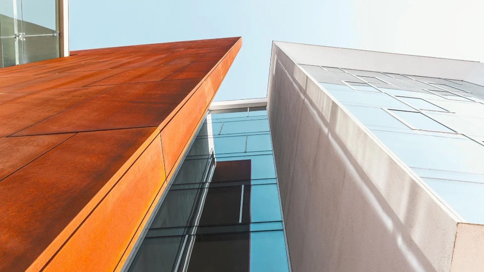 Modern building facades in rust-orange steel and reflective glass converging upward, symbolizing two perspectives on the same business
