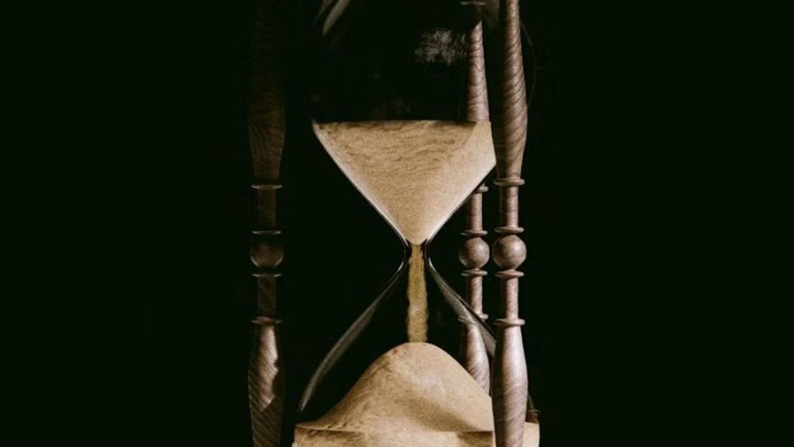 Wooden hourglass with sand flowing, symbolizing payment deadlines and time running out